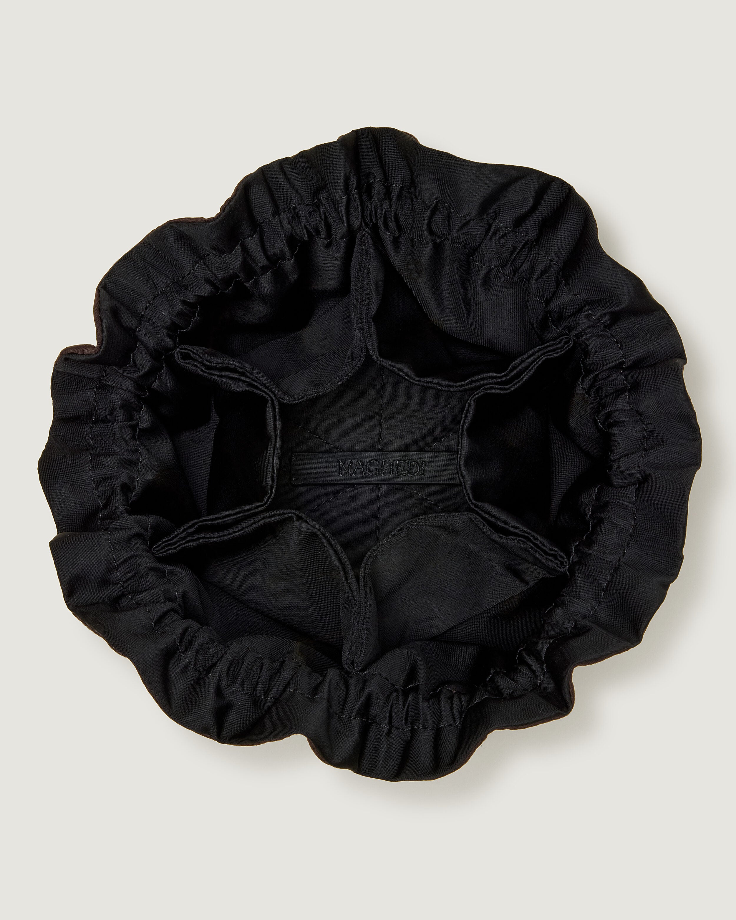 Interior close-up of Lotus Jewelry Pouch in Chocolate showing its drawstring closure, one large center compartment. six small open interior pockets, and contrast neoprene interior.