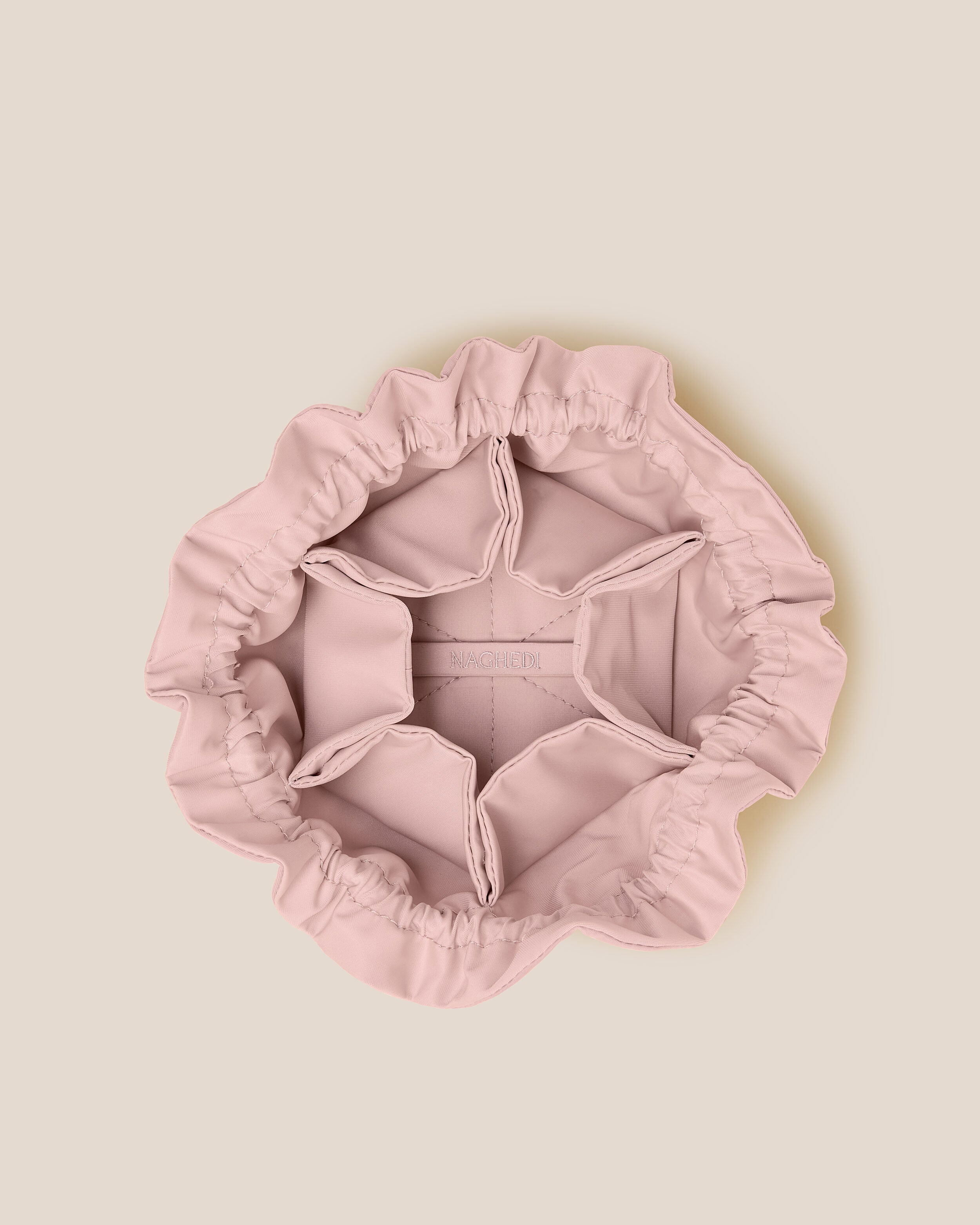 Interior close-up of Lotus Jewelry Pouch in Petal showing its drawstring closure, one large center compartment. six small open interior pockets, and contrast neoprene interior.