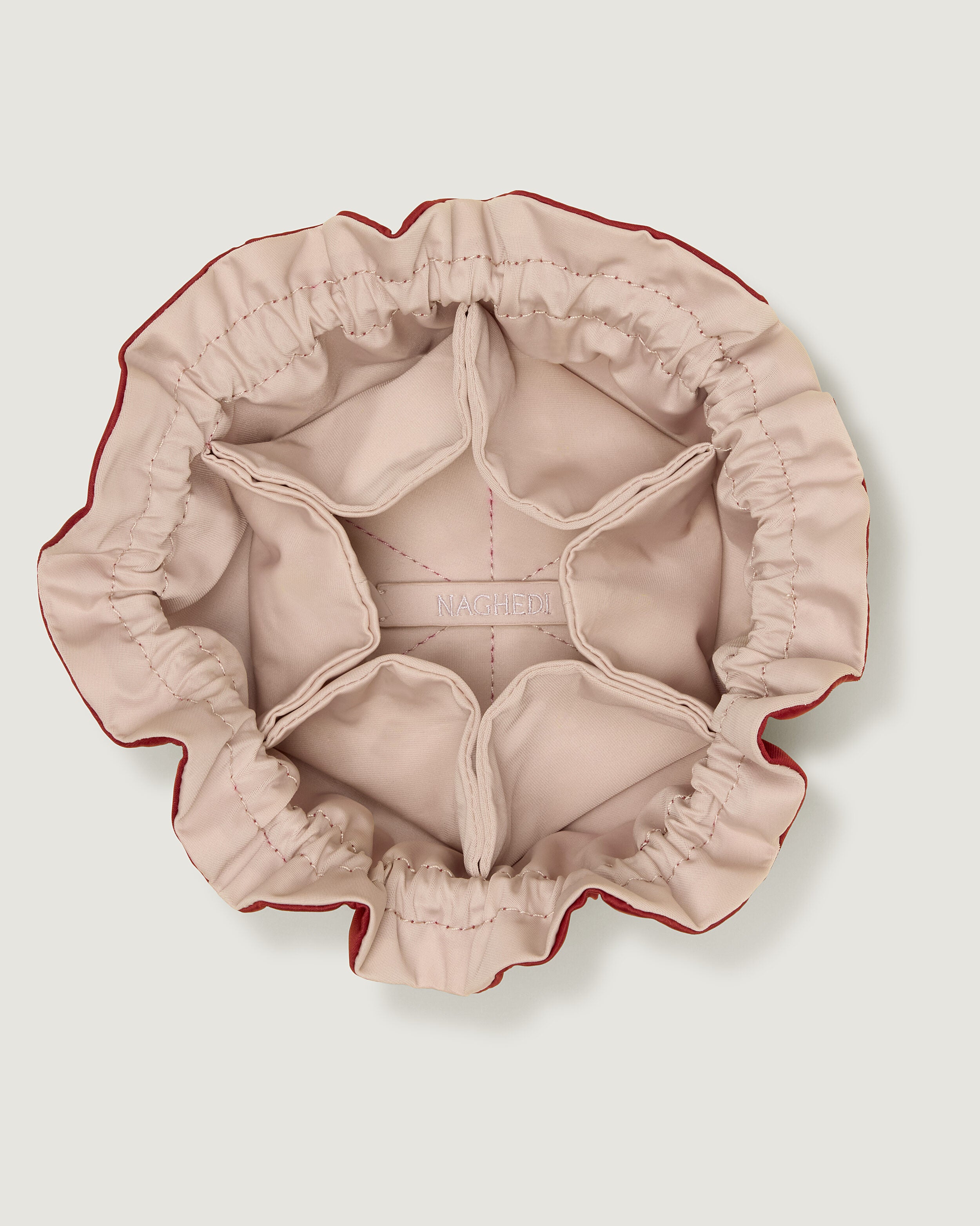 Interior close-up of Lotus Jewelry Pouch in Rosso (Lotus) showing its drawstring closure, one large center compartment. six small open interior pockets, and contrast neoprene interior.