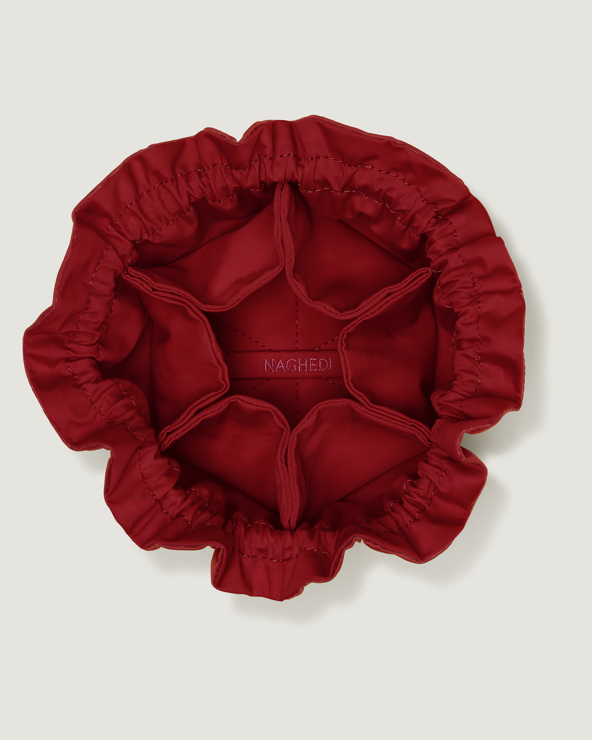 Interior close-up of Lotus Jewelry Pouch in Rosso showing its drawstring closure, one large center compartment. six small open interior pockets, and contrast neoprene interior.
