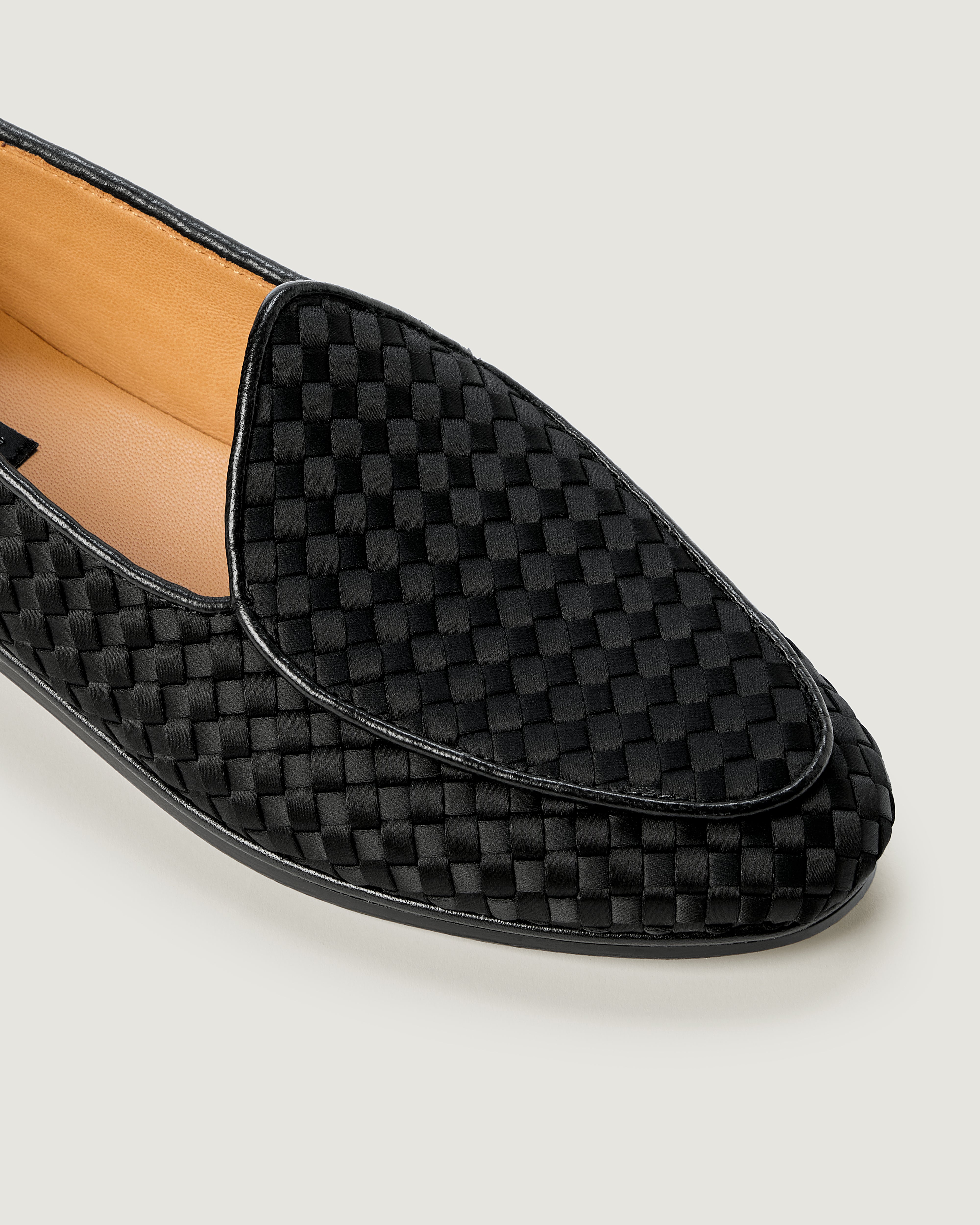 A close up of a single black handwoven satin loafer with leather trim.