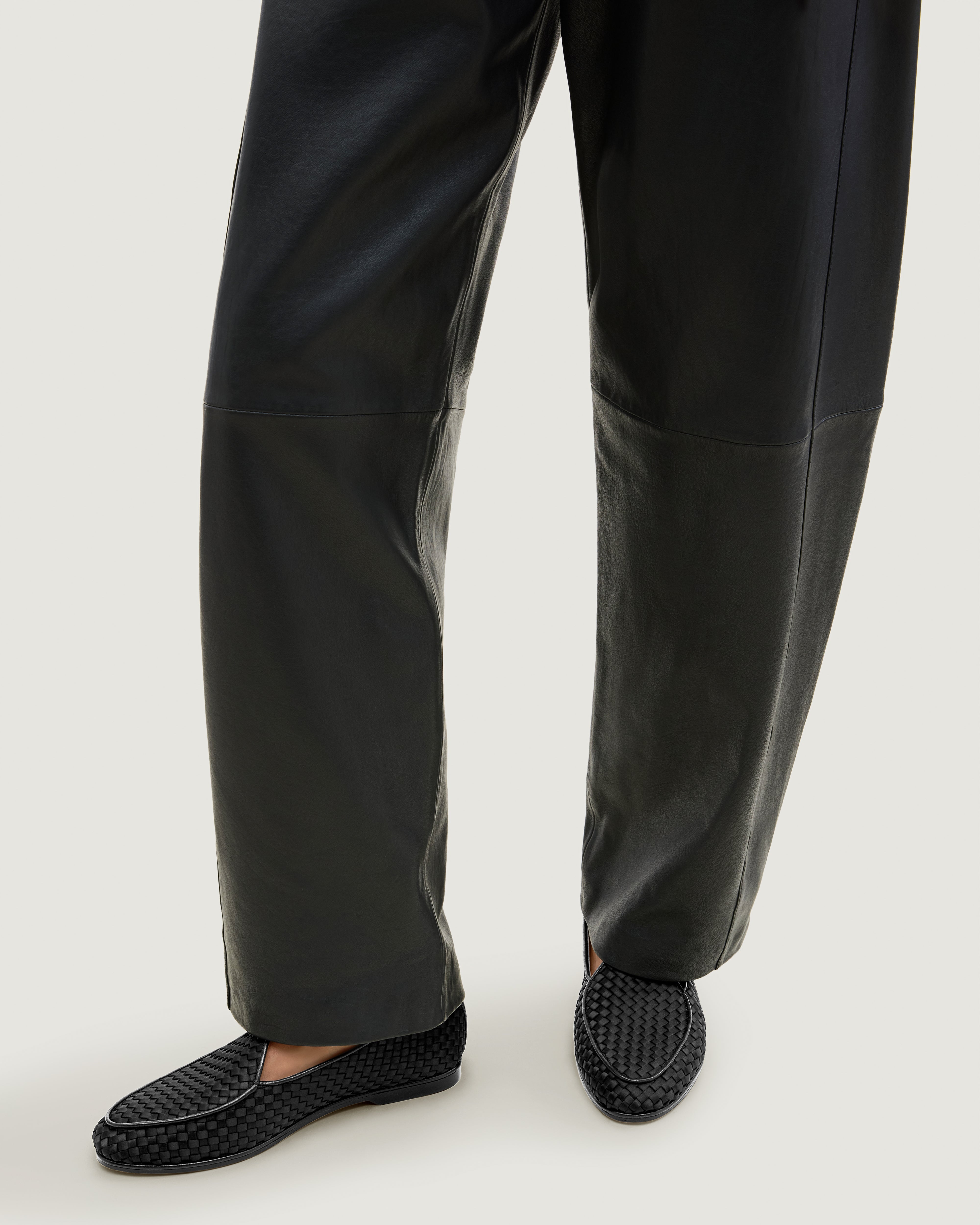 Model wearing handwoven satin slip-on loafers against a light gray background.