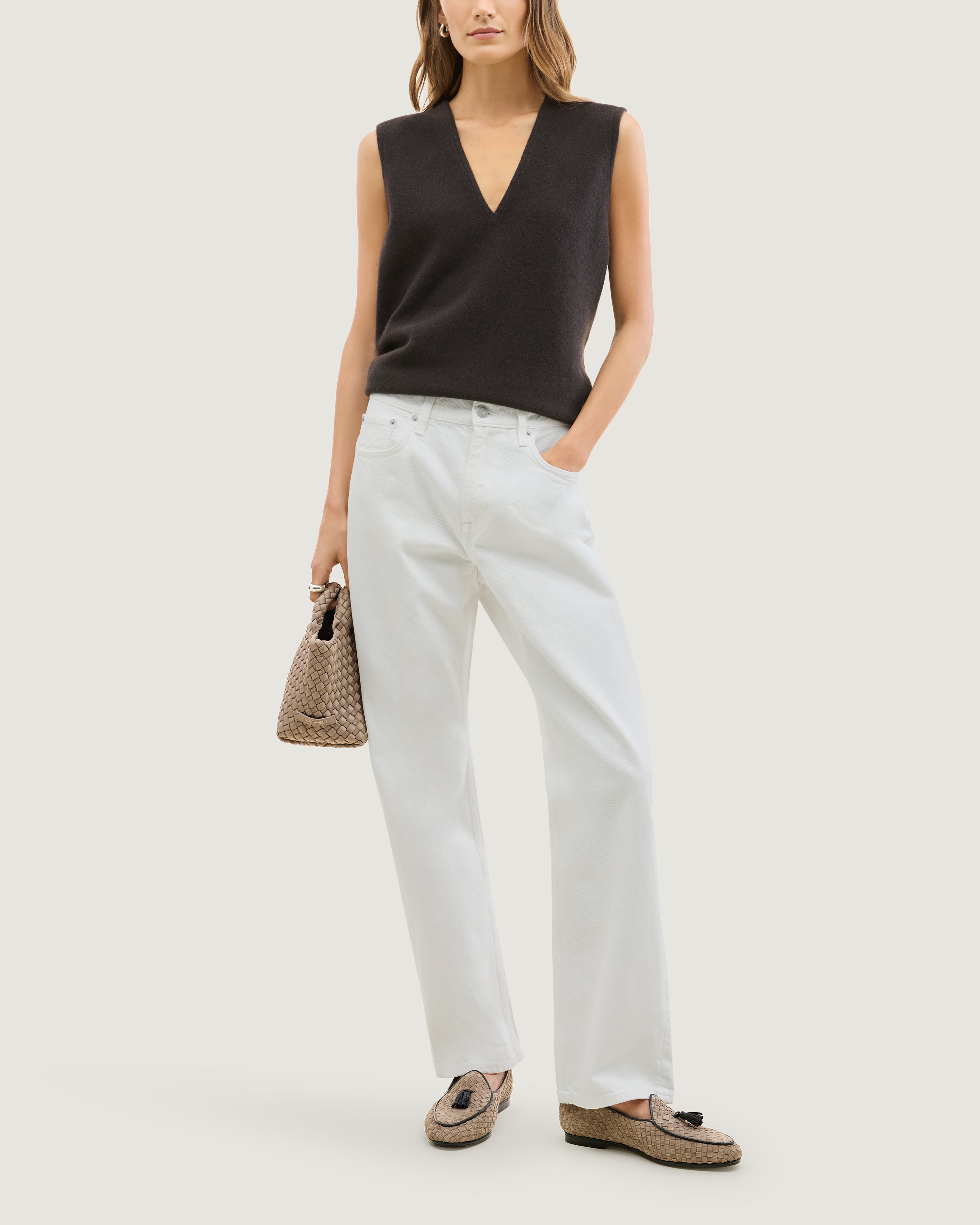 Full body shot of a model wearing a pair of suede loafers in beige with a black tassel and black trim.