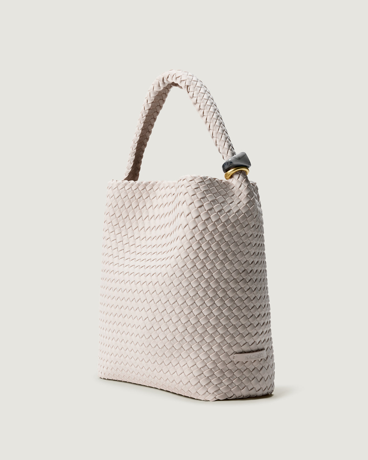 Nomad Hobo in Linen shown from a side angle, highlighting its handwoven neoprene construction, sculptural bead ornaments, and open top with magnetic snap closure.