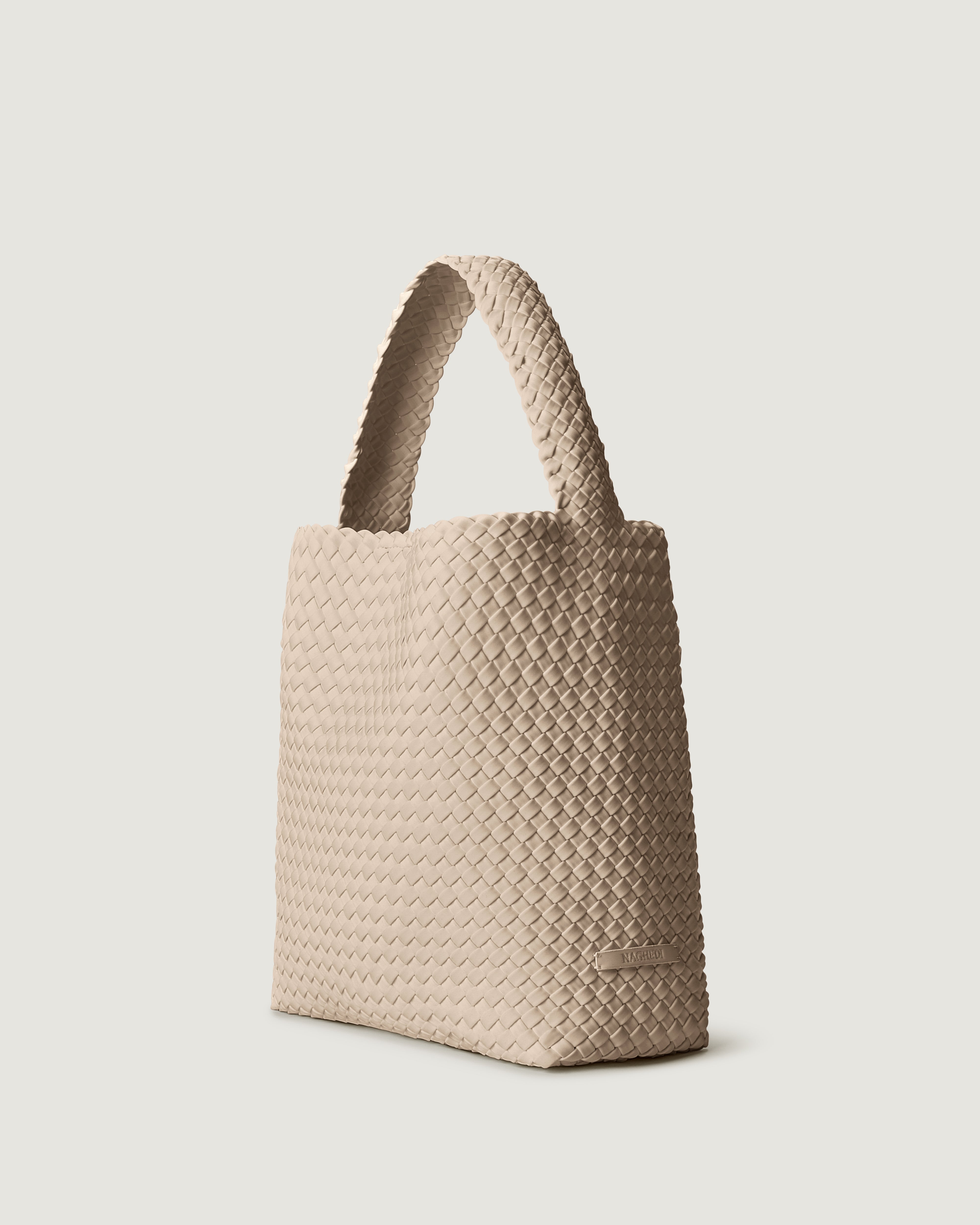 Nomad Hobo in Ecru shown from a side angle, highlighting its handwoven neoprene construction and open top with magnetic snap closure.