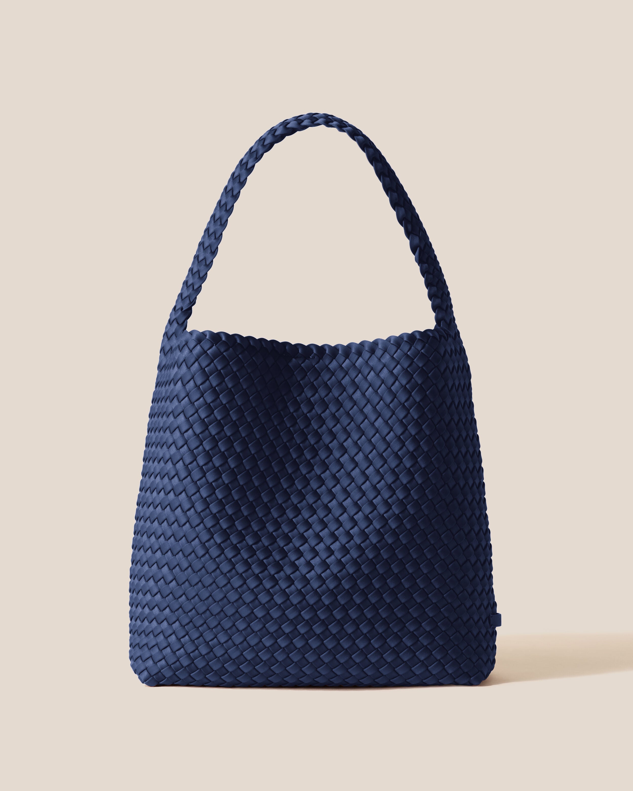 Nomad Hobo in Ink Blue, a navy blue tone, in handwoven neoprene, featuring an open top with magnetic snap closure, and handwoven shoulder strap lays comfortably flat.