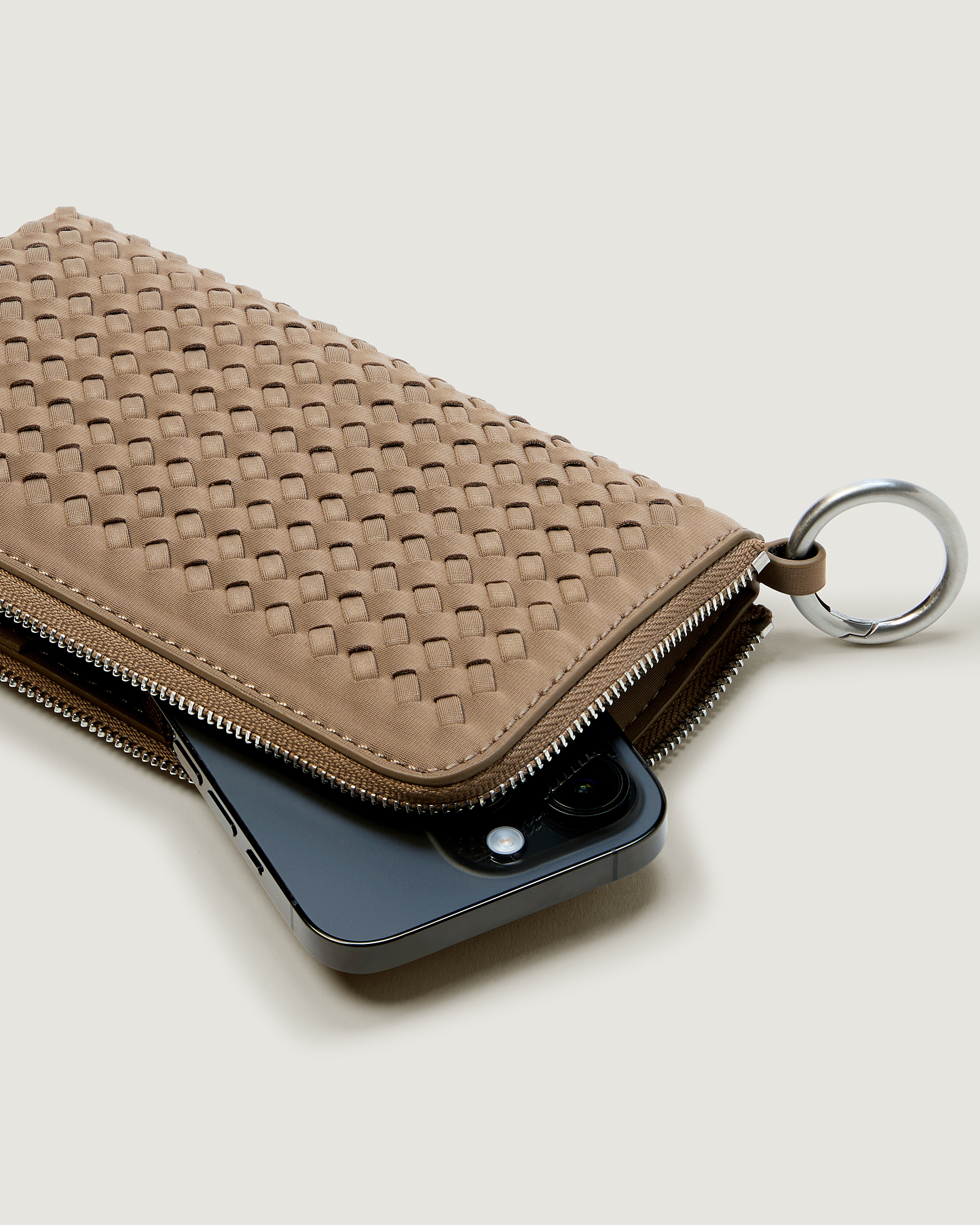 A handwoven neoprene crossbody zippered phone case in a taupe-brown color, with an iPhone inside.