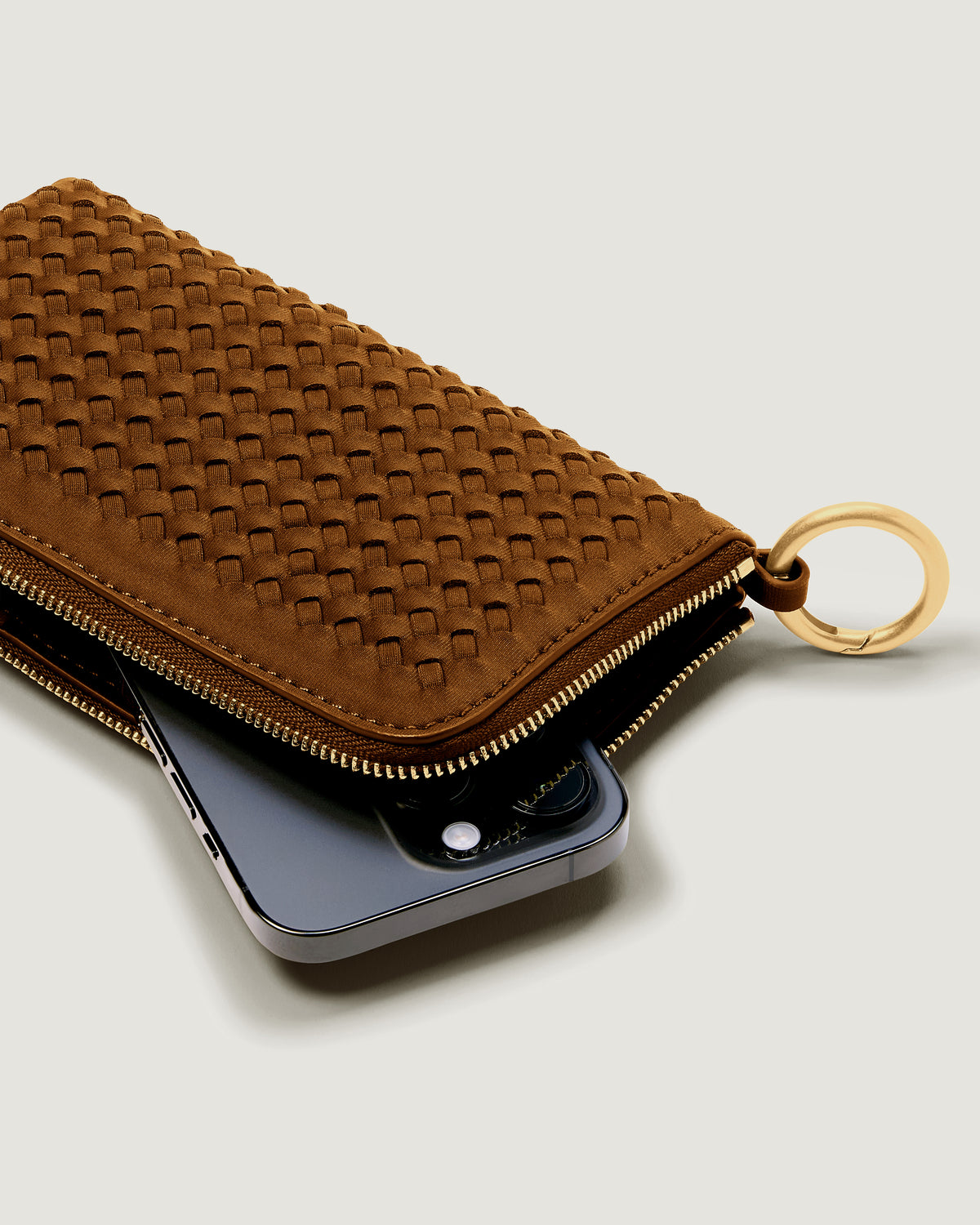 A handwoven neoprene crossbody zippered phone case in a taupe-brown color, with an iPhone inside.