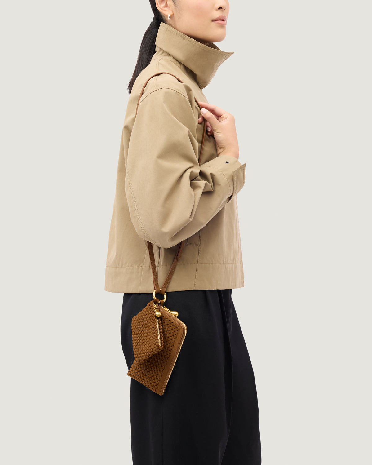 Model wearing a handwoven neoprene crossbody zippered phone case in a saddle brown color, featuring a matching zippered card holder pouch and a thin adjustable shoulder strap.