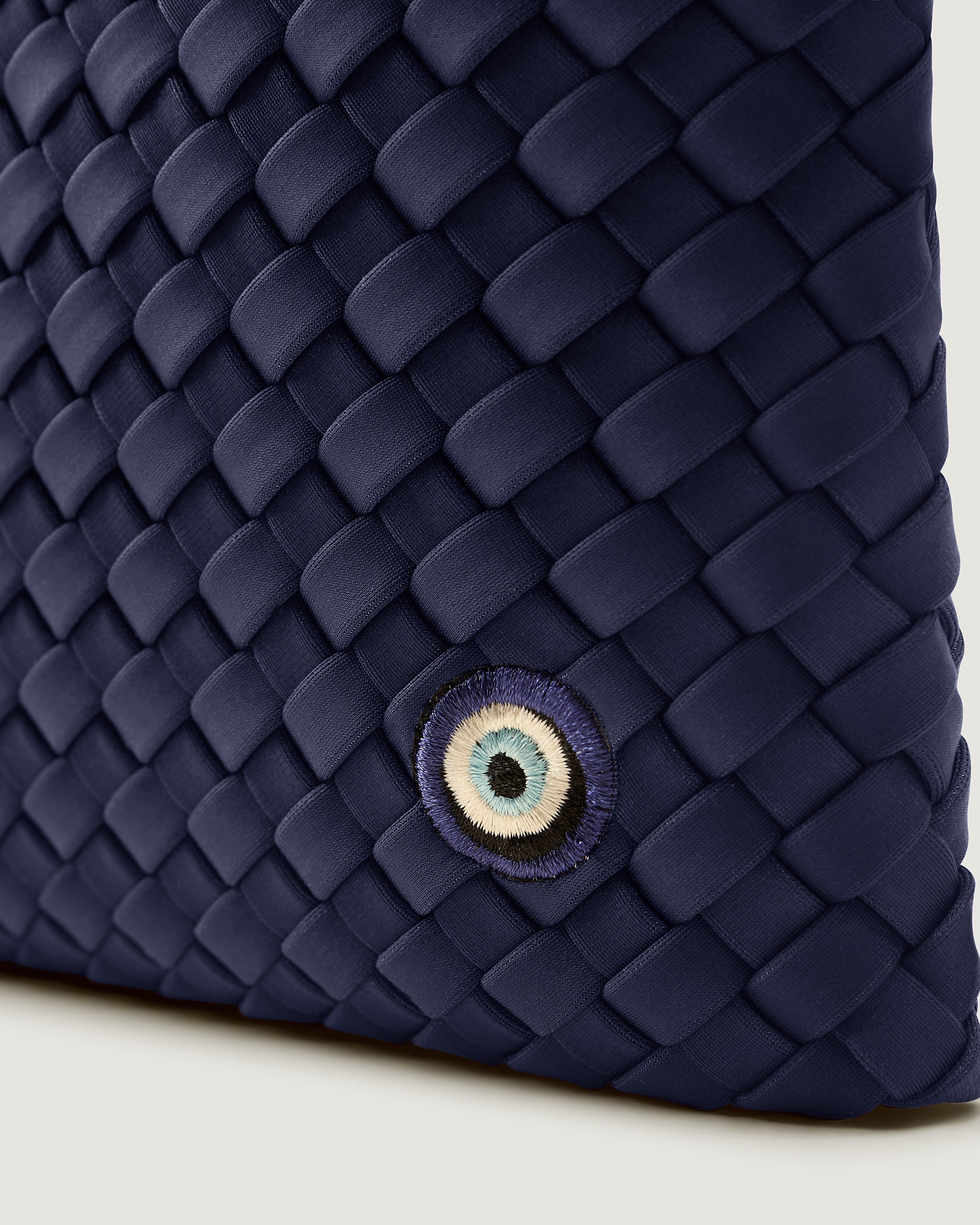 Close up of Salina Pouch in Ink Blue, highlighting the handwoven neoprene and Evil Eye embroidery.