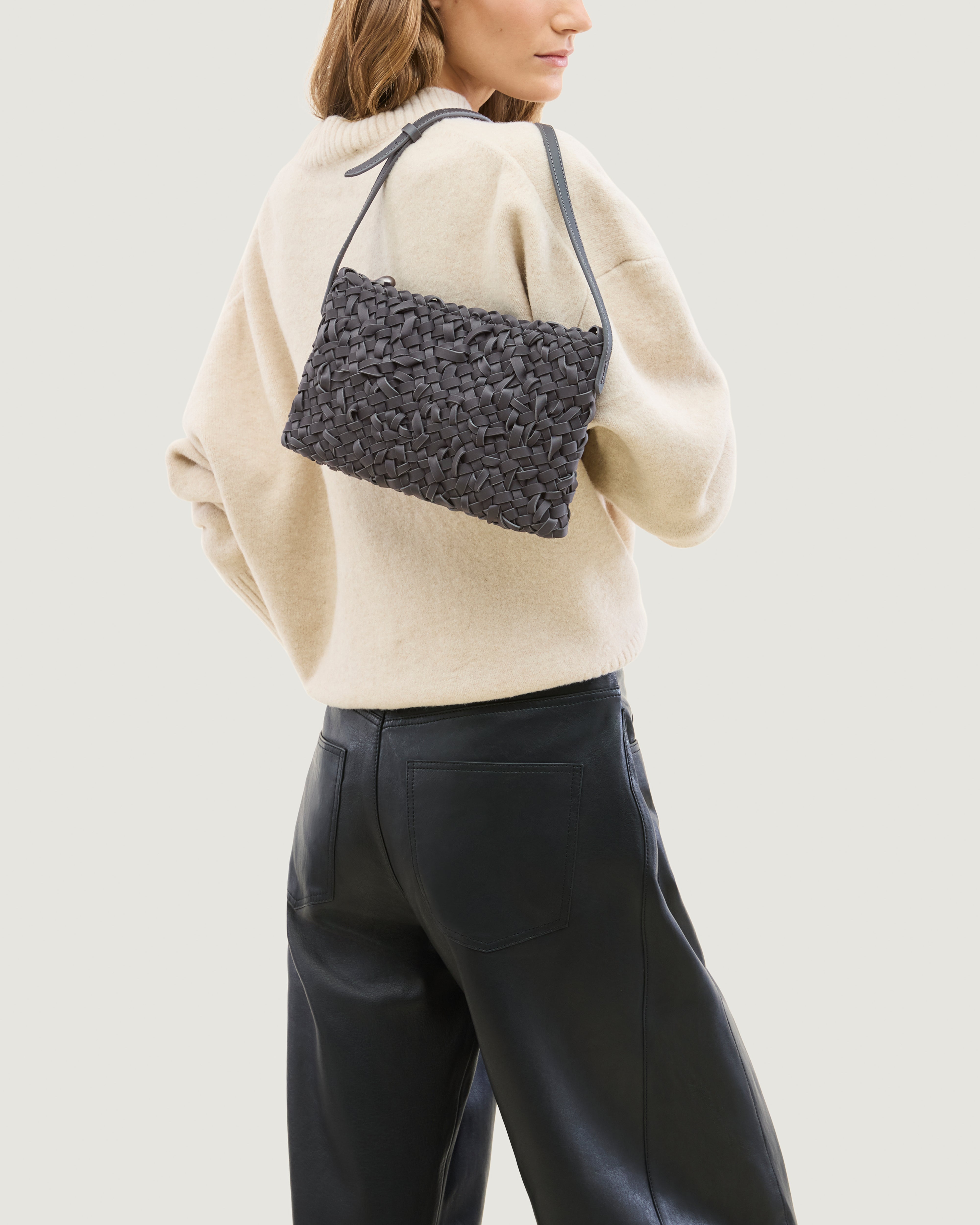 Model holding handwoven neoprene crossbody bag in ash gray color with a crosshatch nest weave pattern