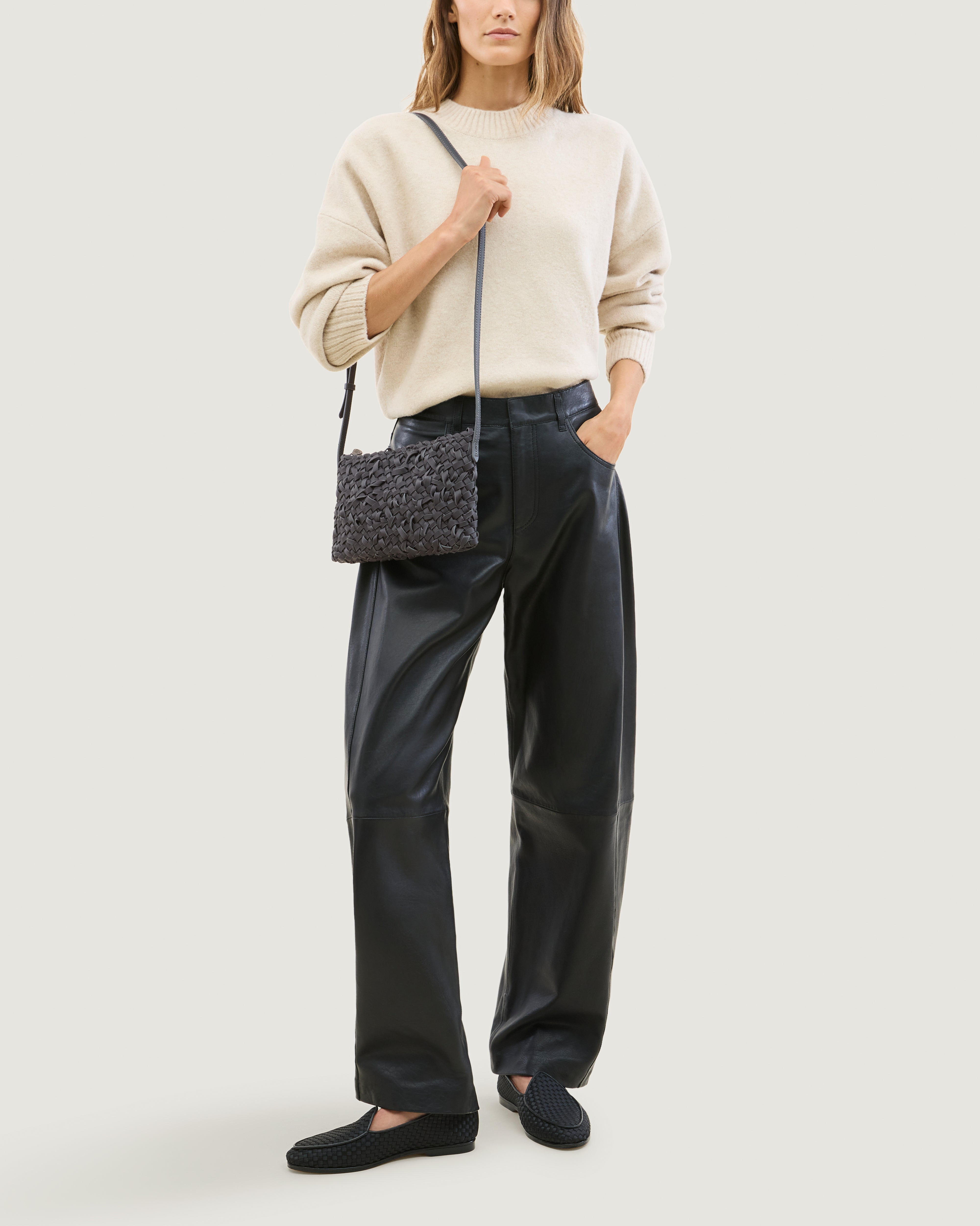 Model wearing handwoven neoprene crossbody bag in ash gray color with a crosshatch nest weave pattern