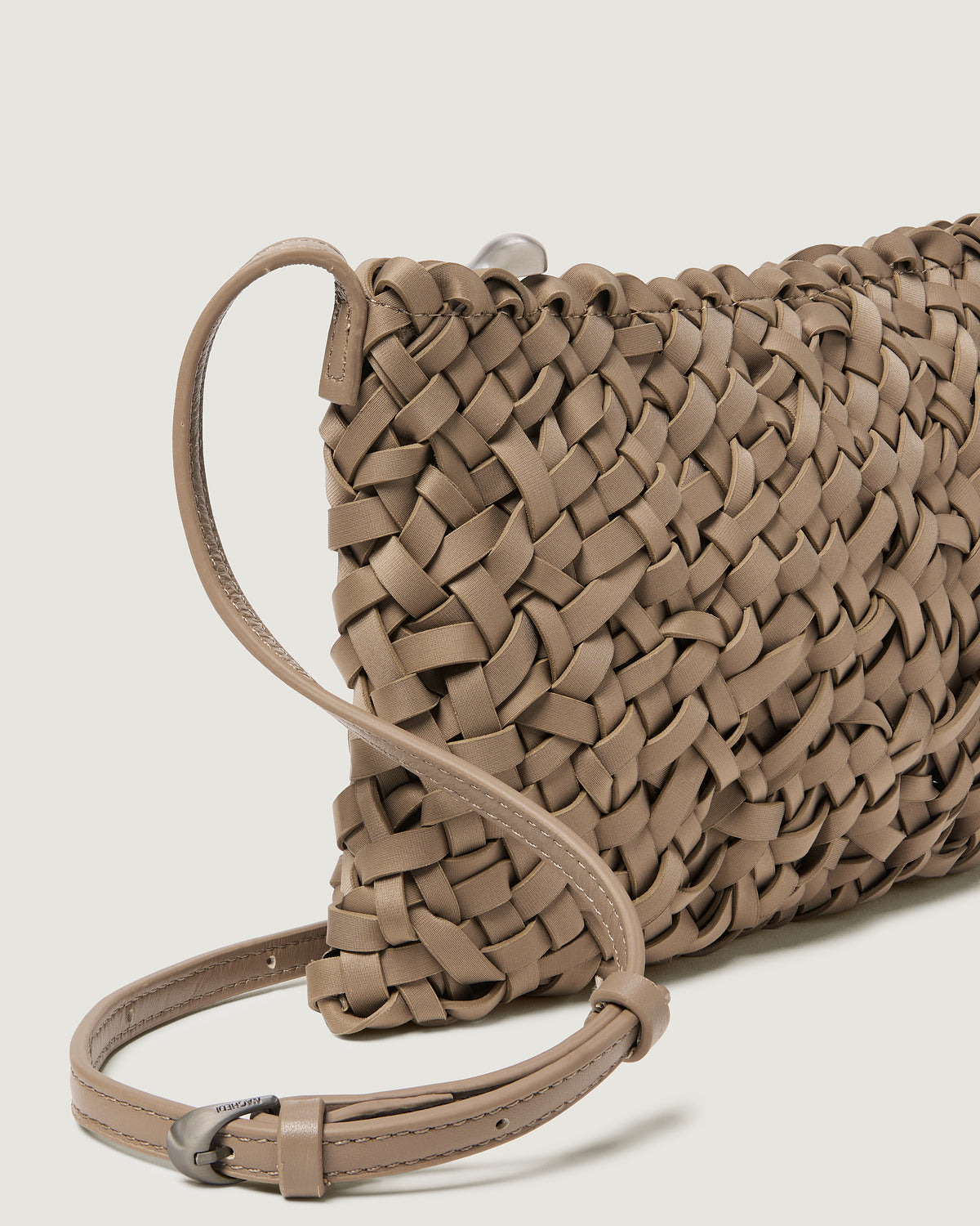 A close-up of a handwoven neoprene crossbody bag in cool taupe color with a crosshatch nest weave pattern