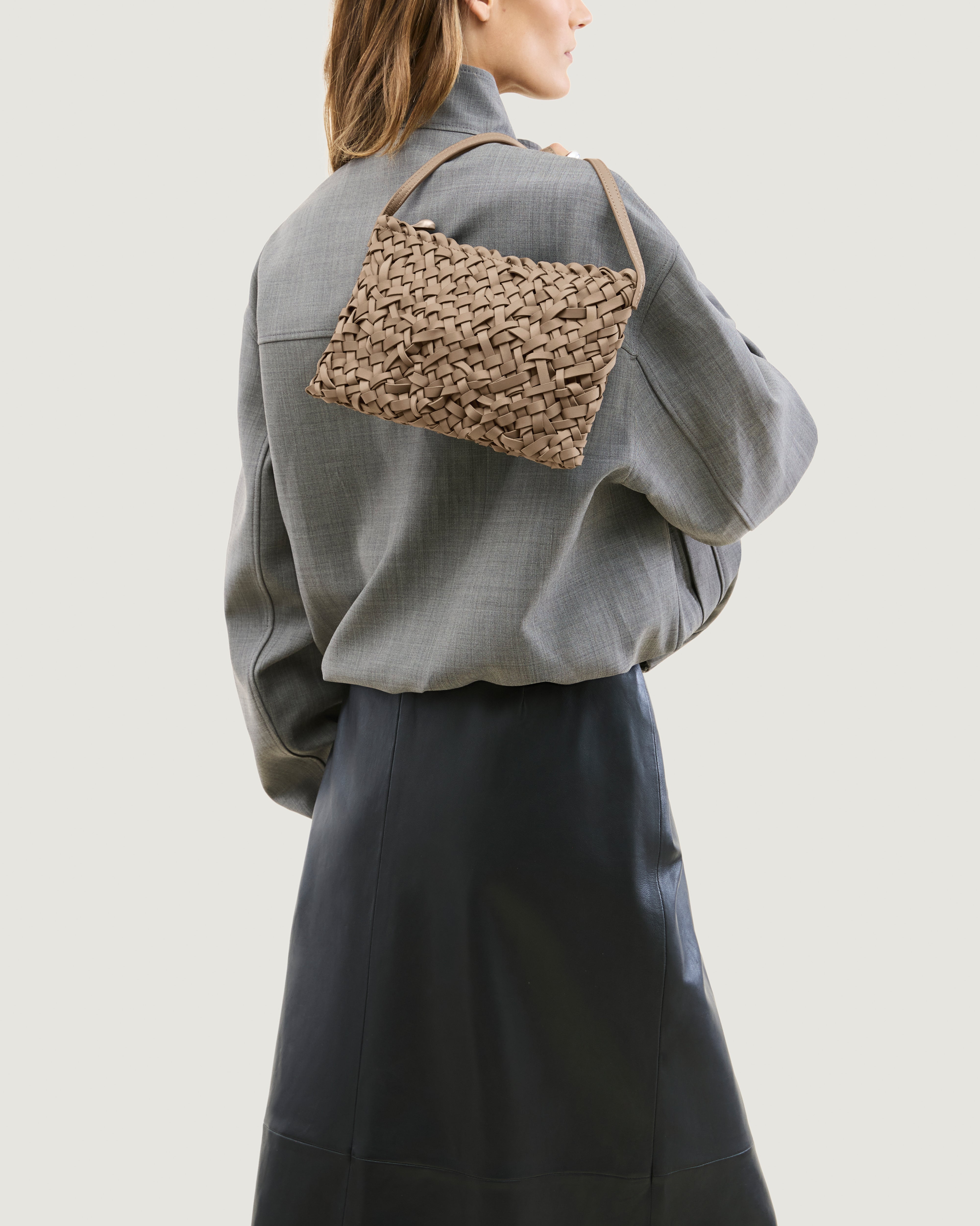 Model holding handwoven neoprene crossbody bag in cool taupe color with a crosshatch nest weave pattern