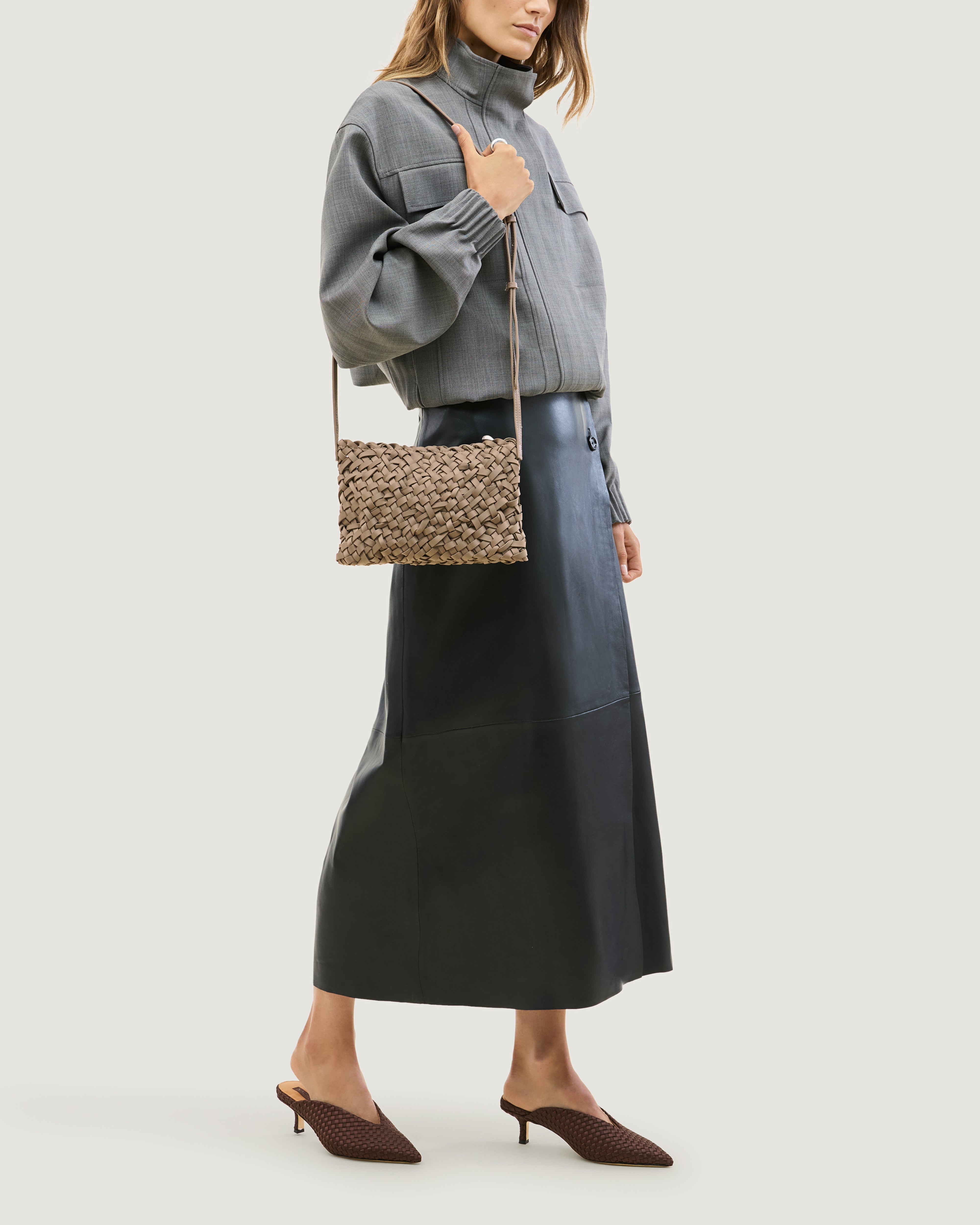 Model wearing handwoven neoprene crossbody bag in cool taupe color with a crosshatch nest weave pattern