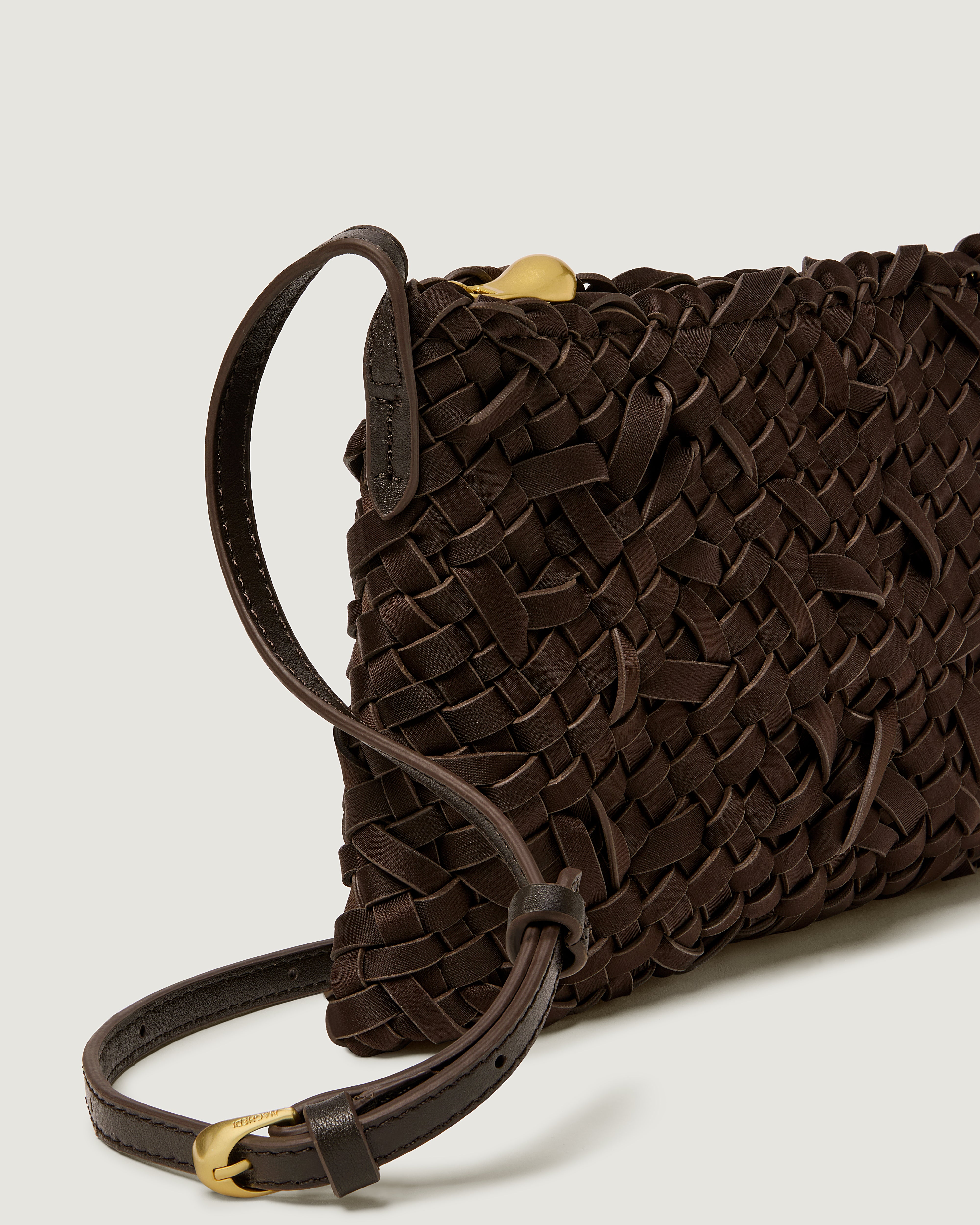 A close-up of a handwoven neoprene crossbody bag in chocolate brown color with a crosshatch nest weave pattern