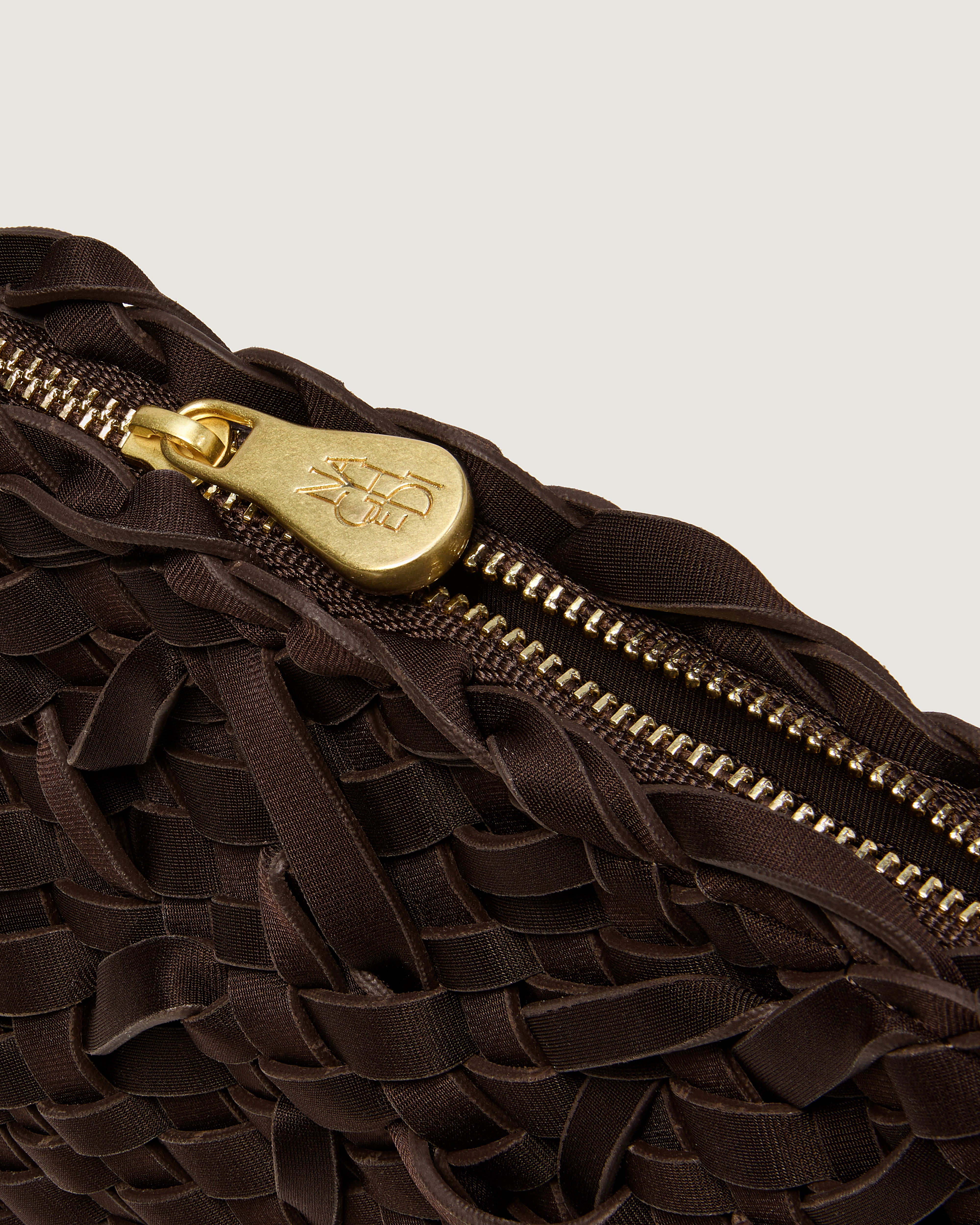 Close up of handwoven neoprene crossbody bag with gold zipper in chocolate brown color.