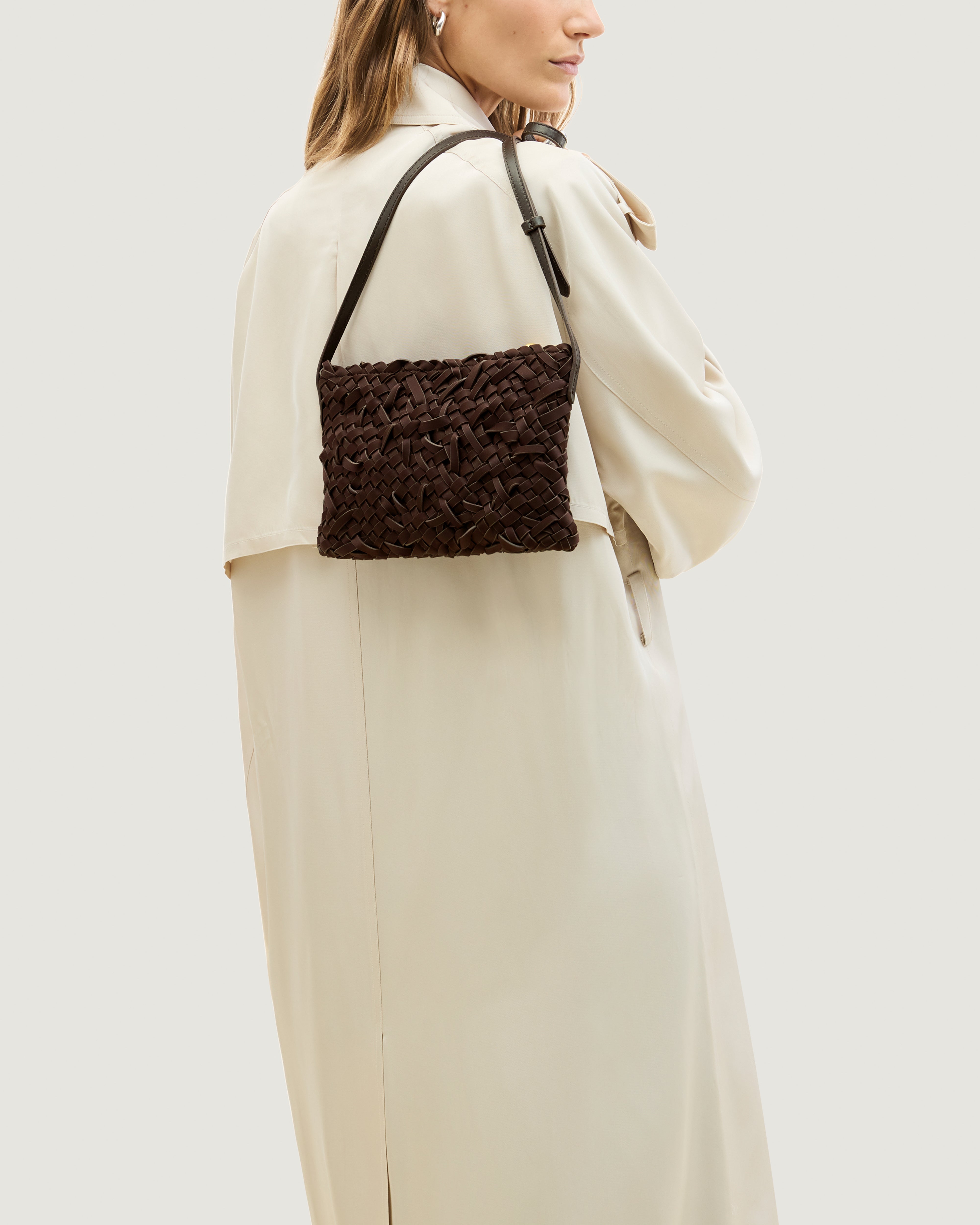Model holding handwoven neoprene crossbody bag in chocolate brown color with a crosshatch nest weave pattern