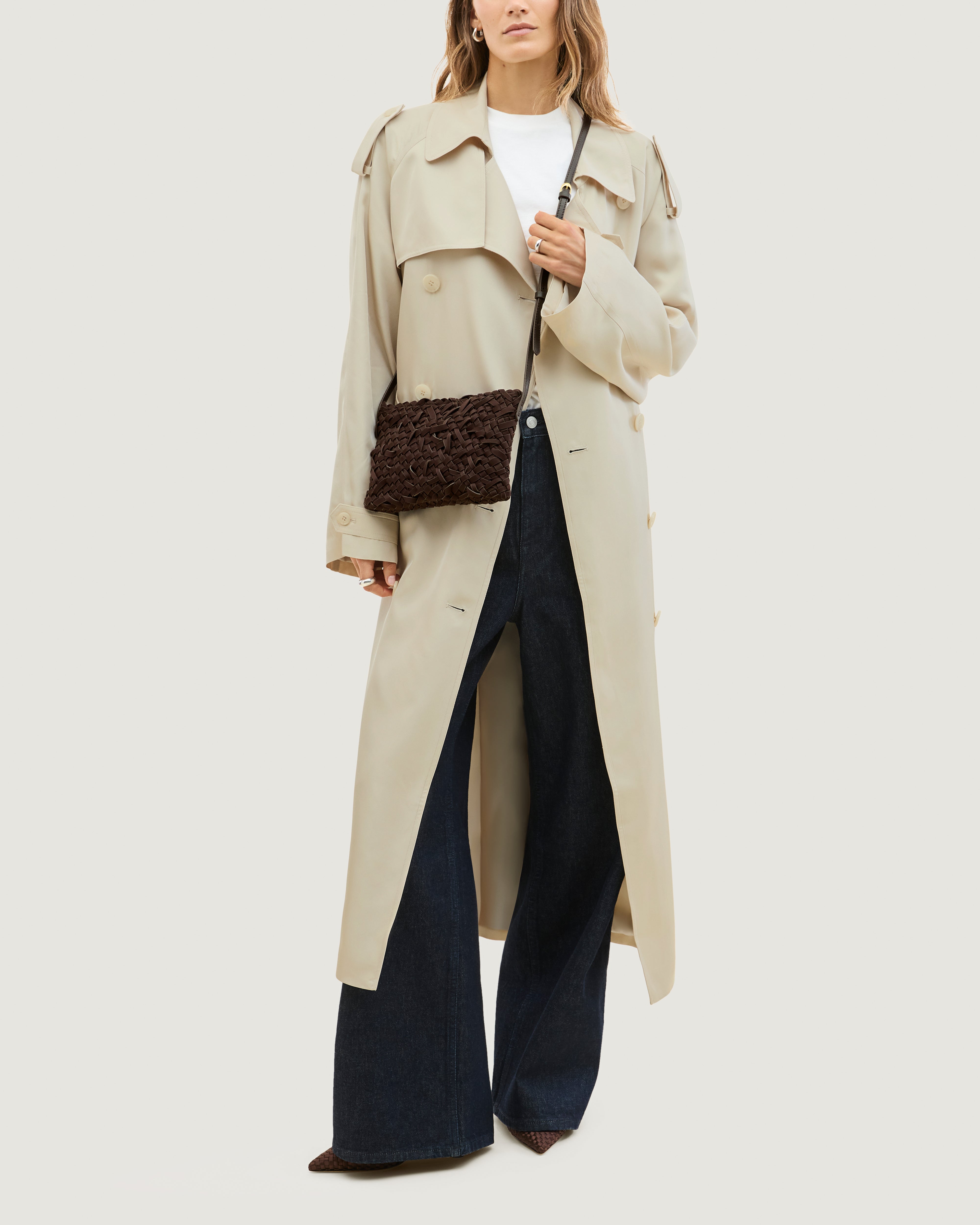 Model wearing handwoven neoprene crossbody bag in chocolate brown color with a crosshatch nest weave pattern