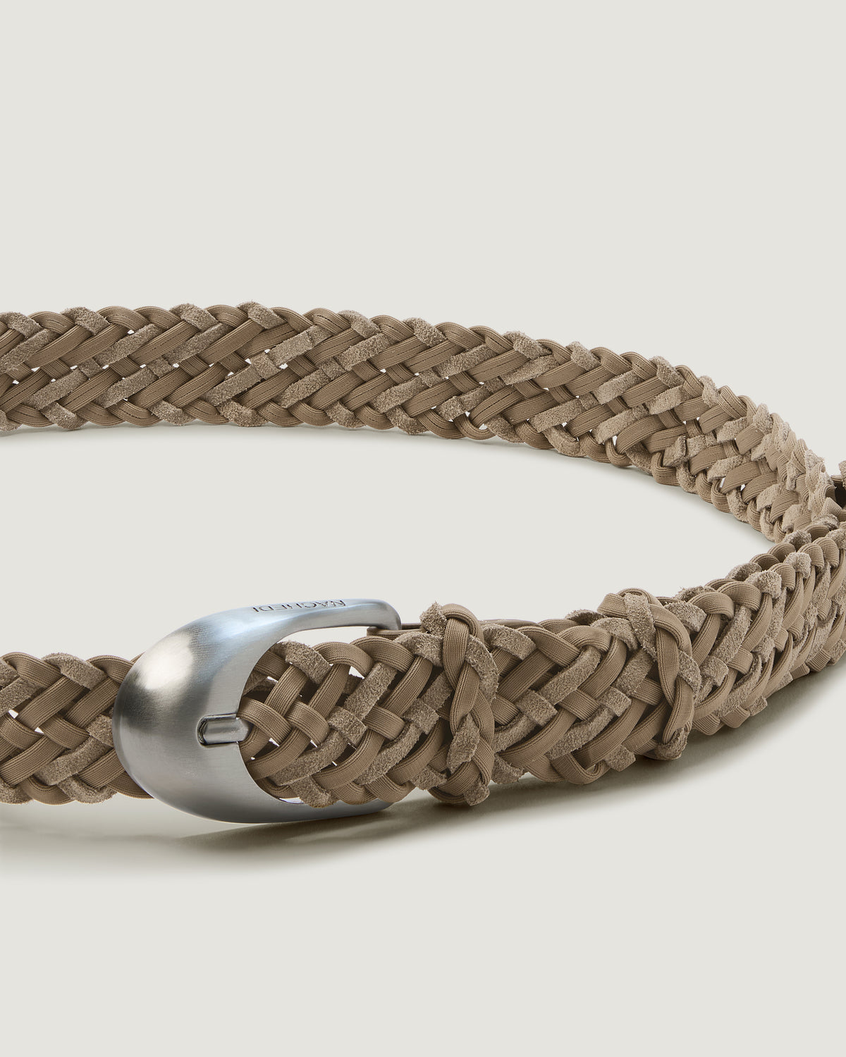 A close-up of a handwoven cool taupe suede and neoprene belt with a polished silver buckle.