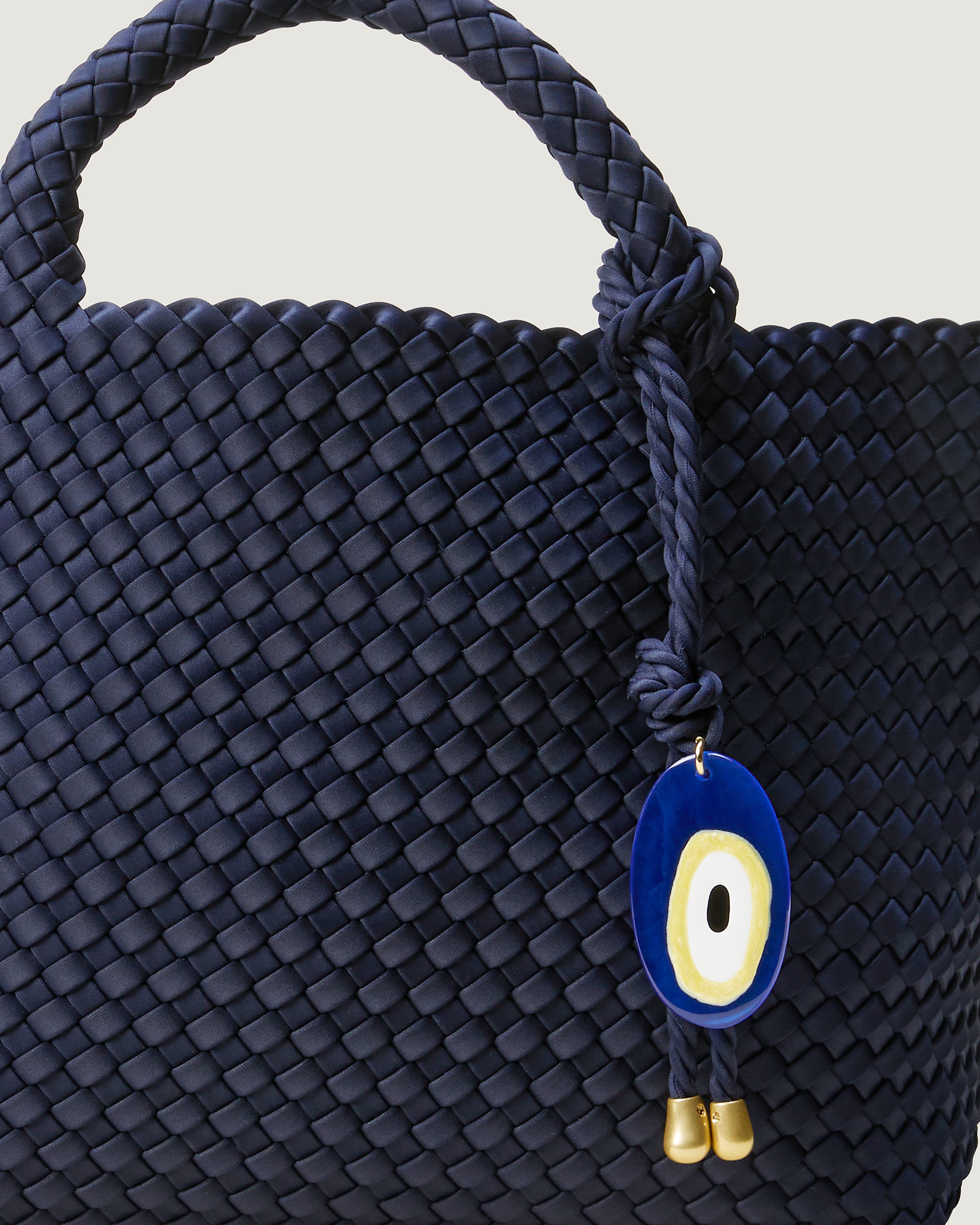 Close up of St. Barths Tote in Ink Blue highlighting its handwoven neoprene construction, open top, and Evil Eye Charm.