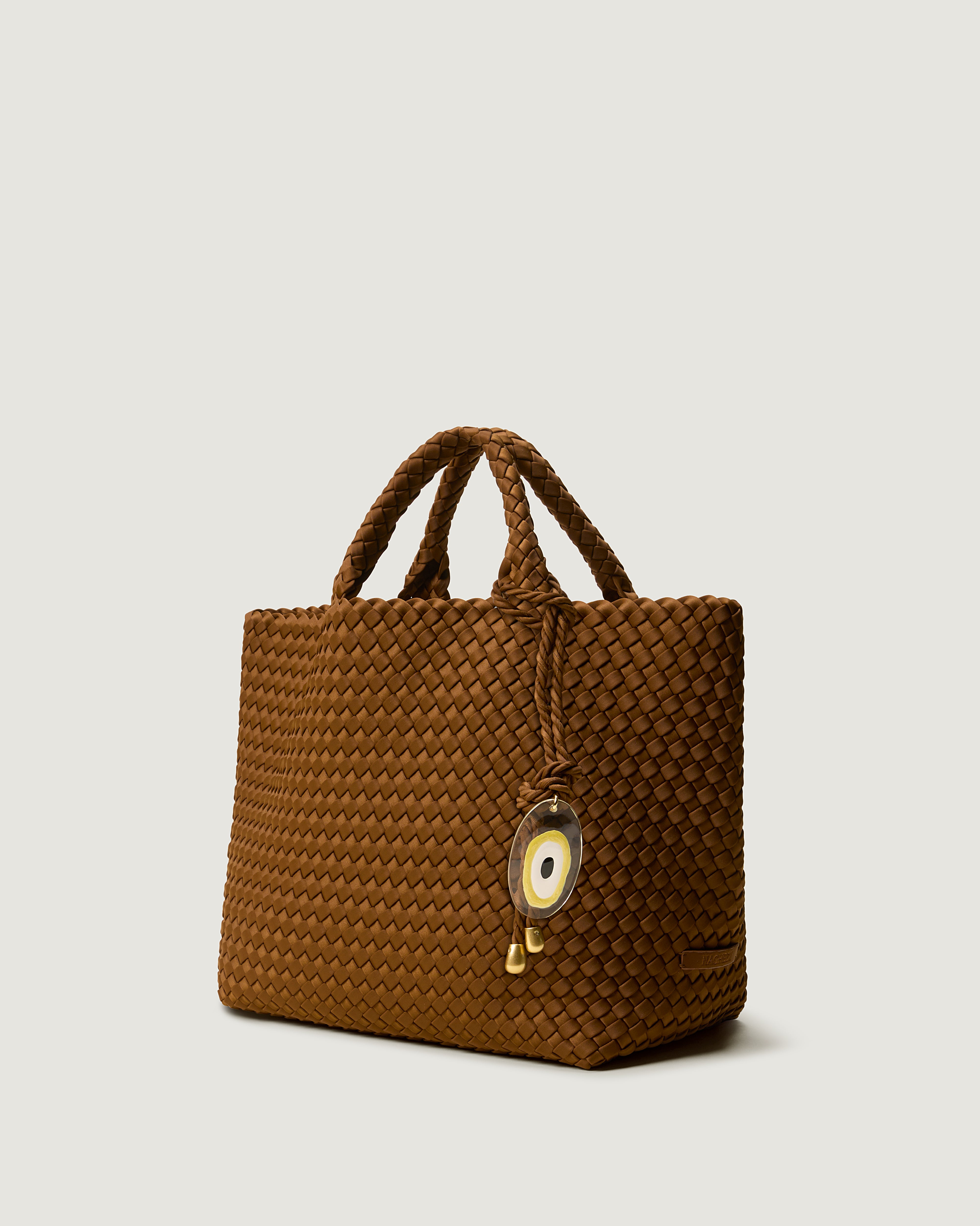 St. Barths Tote in Teak shown from a side angle, highlighting its handwoven neoprene construction, open top, and Evil Eye Charm.