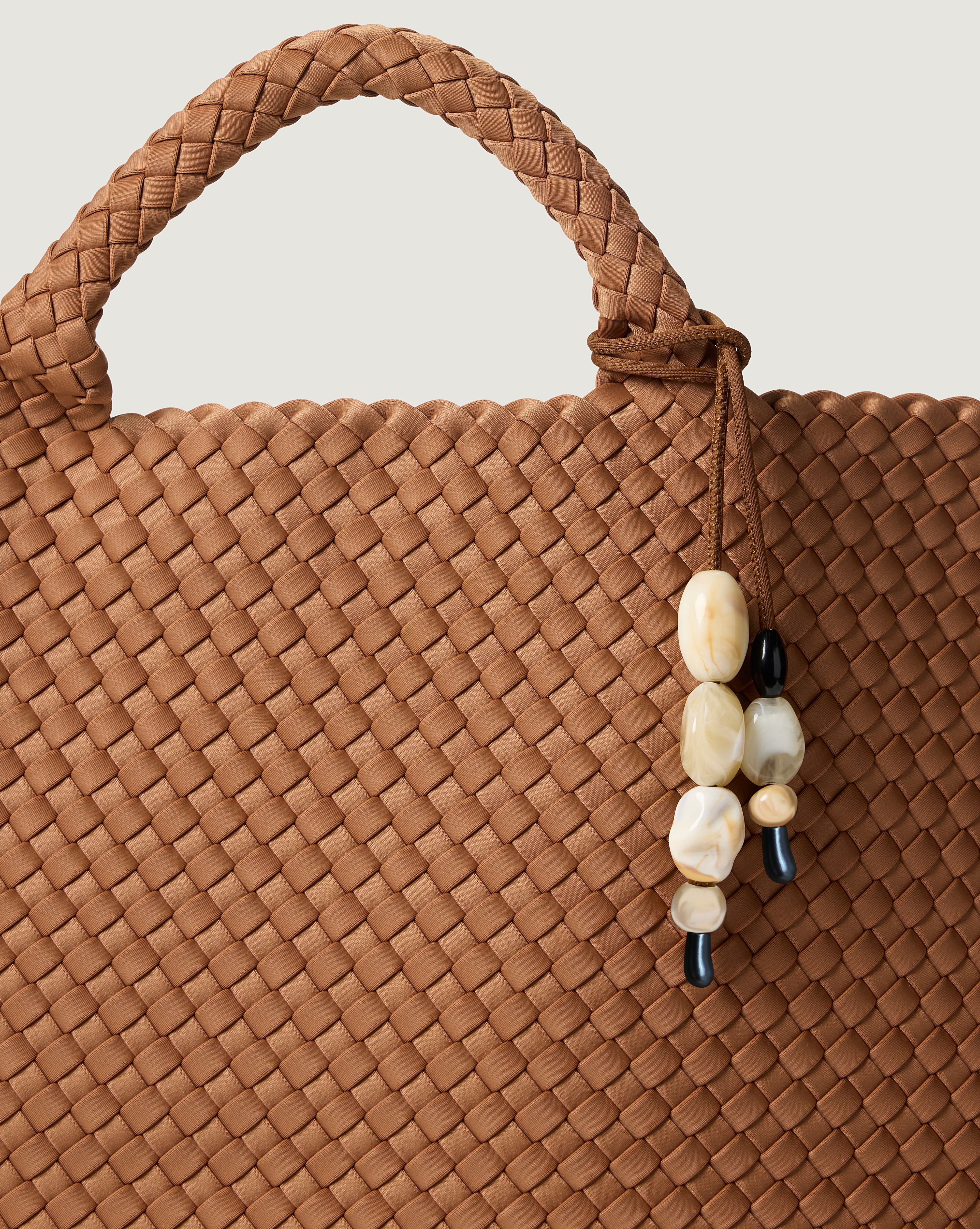 Close up shot of included removable beaded charm on the handwoven neoprene tote bag in mocha brown tone