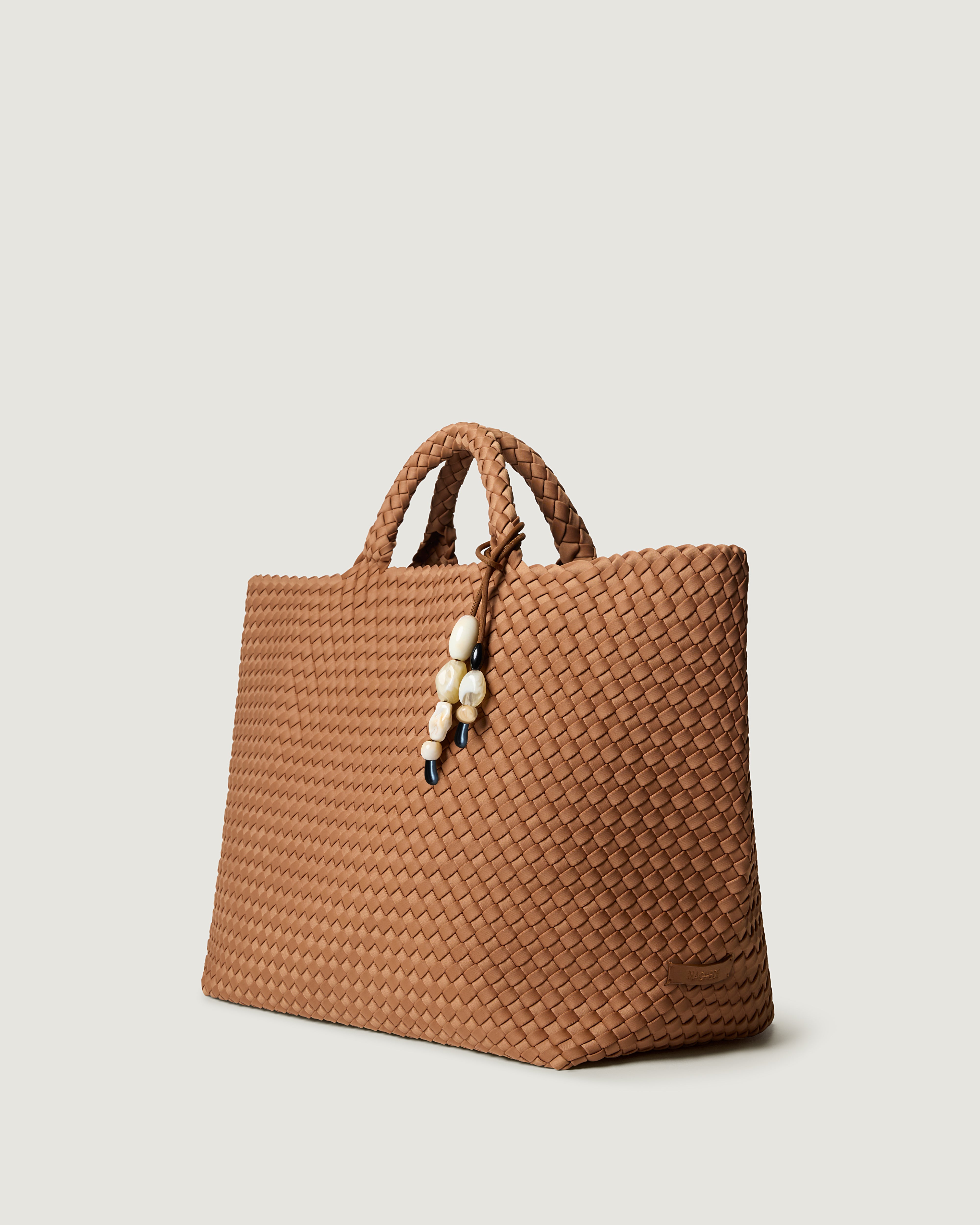 Side view of St. Barths Tote in Cocoa, a mocha brown tone, in handwoven neoprene, featuring an removable bead charm, open top, and woven top handles.