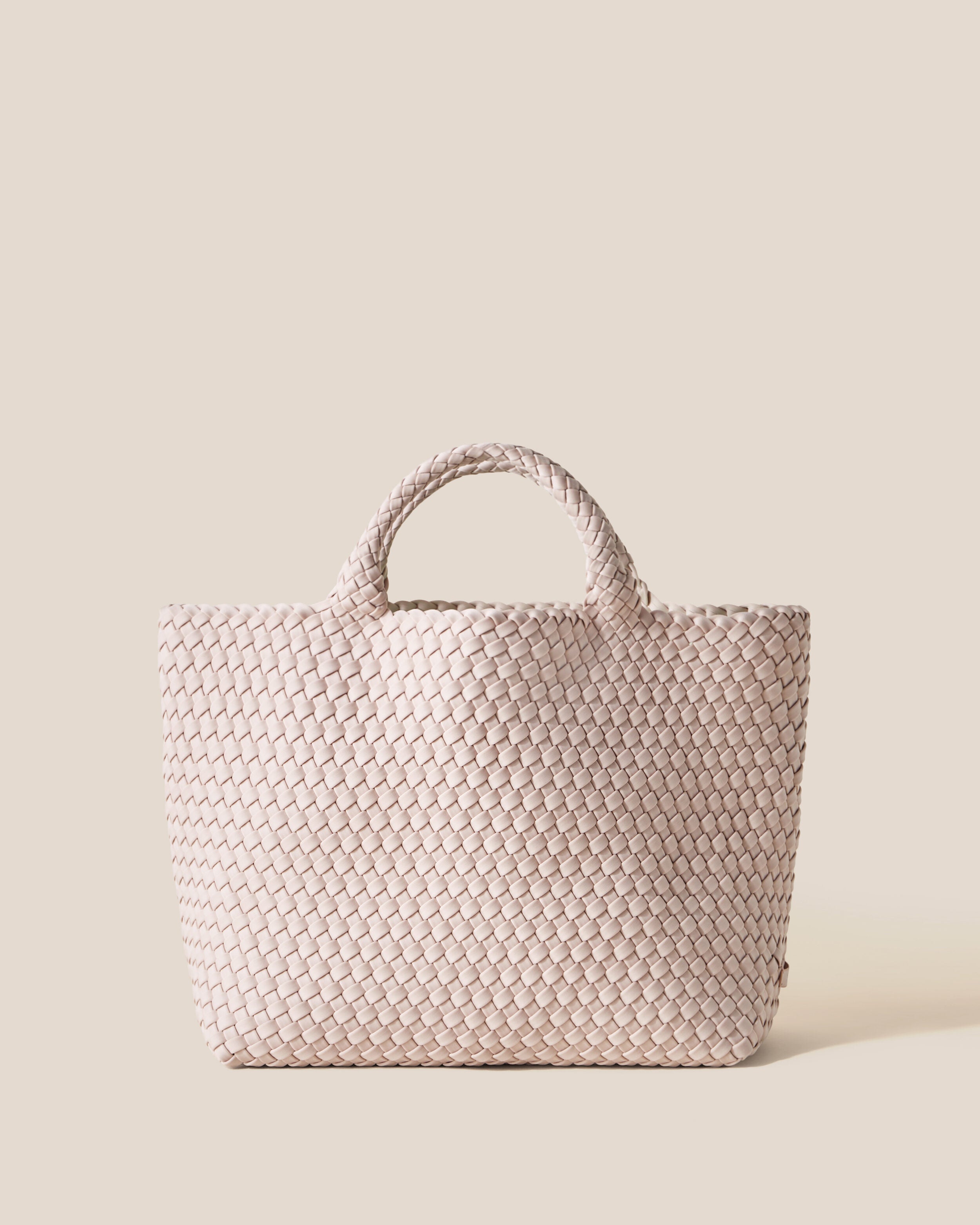 St. Barths Tote in Shell Pink, a soft ballet pink tone, in handwoven neoprene, featuring an open top, and woven top handles.