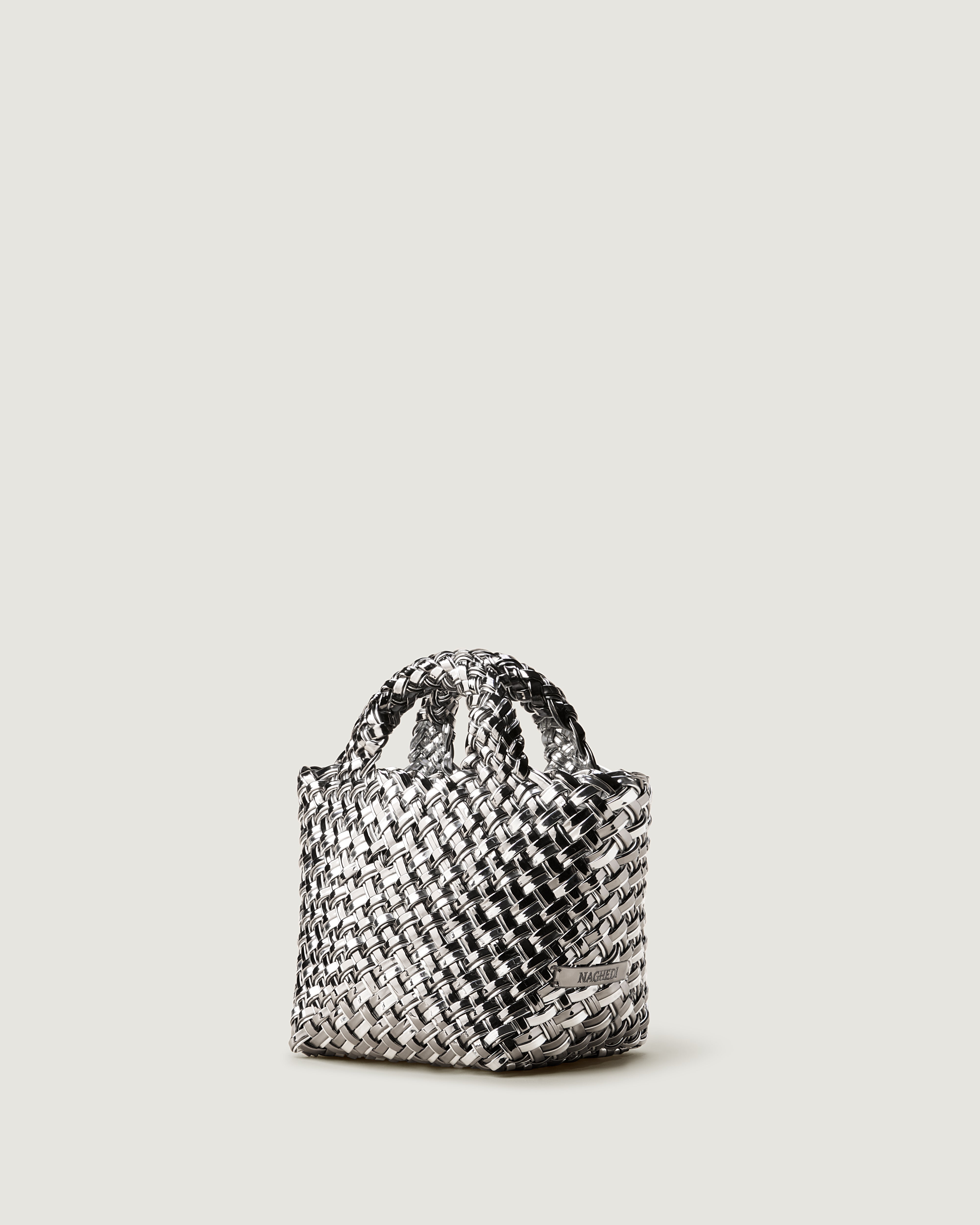 St. Barths Tote in Pewter shown from a side angle, highlighting its handwoven metallic-coated nylon construction and open top.