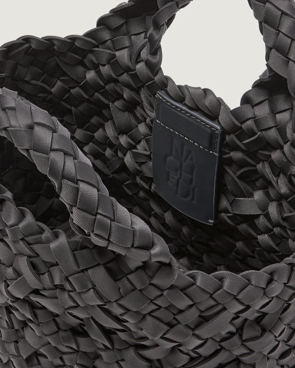 Close-up of an ash gray woven basket-style neoprene handbag with a top handle and a leather shoulder strap.