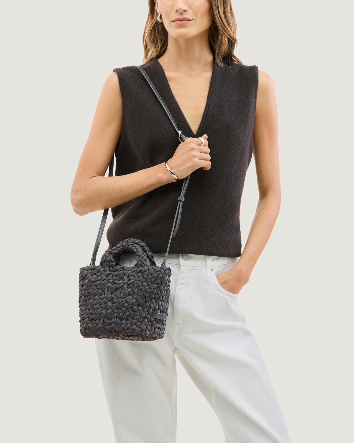 Model wearing a n ash gray woven basket-style neoprene handbag with a top handle and a leather shoulder strap.