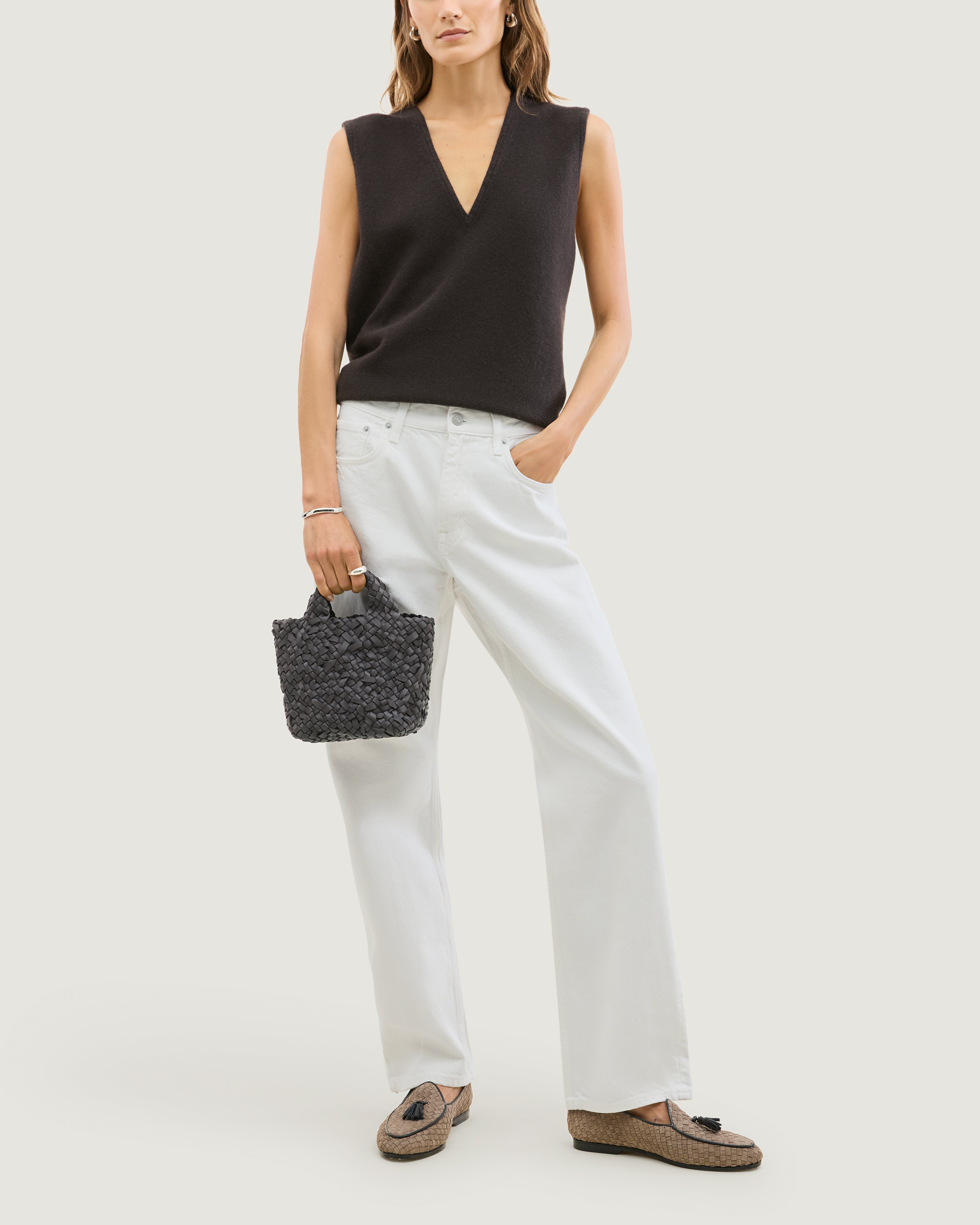 Model holding an ash gray woven basket-style neoprene handbag with a top handle.