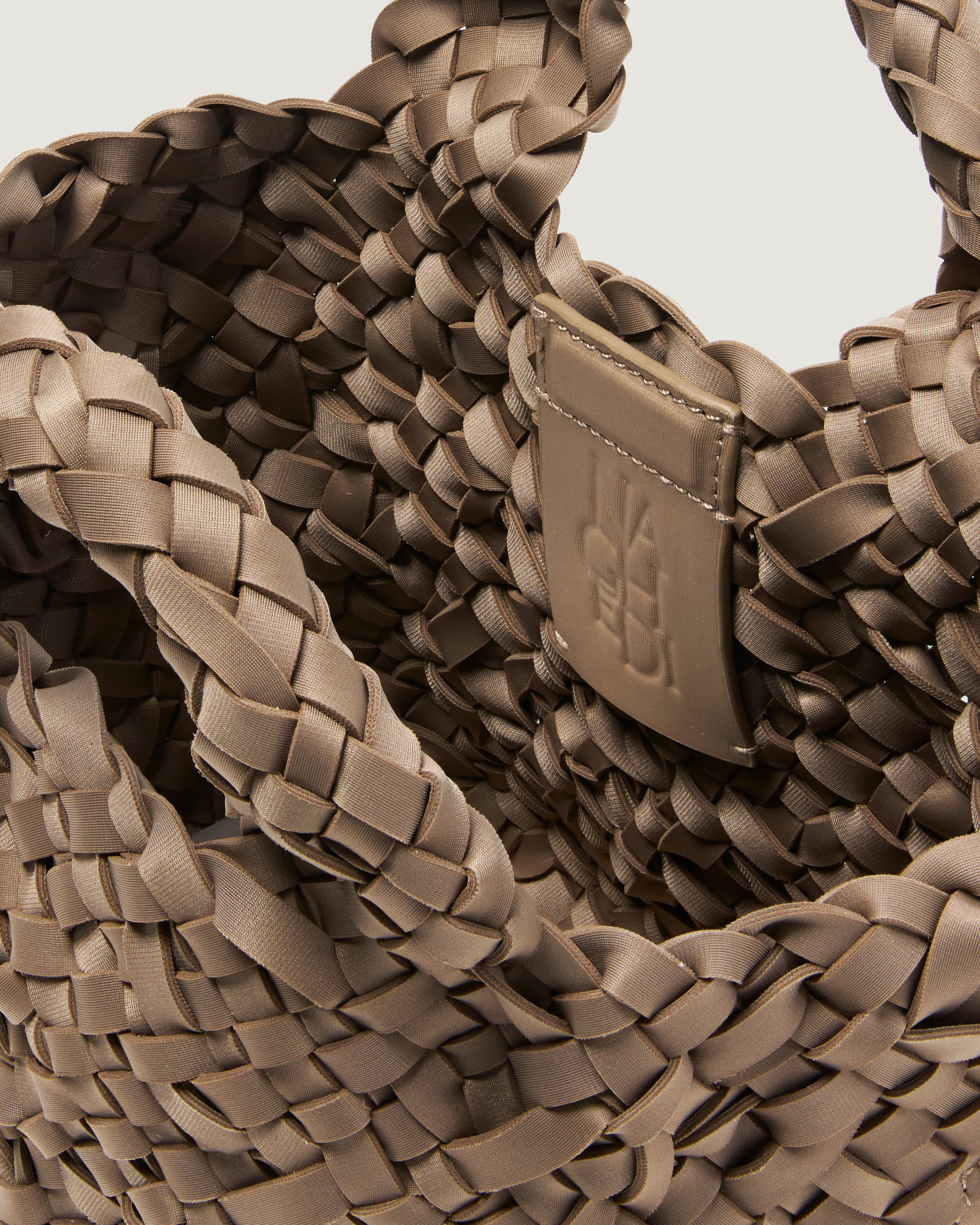 Close-up of a cool taupe woven basket-style neoprene handbag with a top handle and a leather shoulder strap.