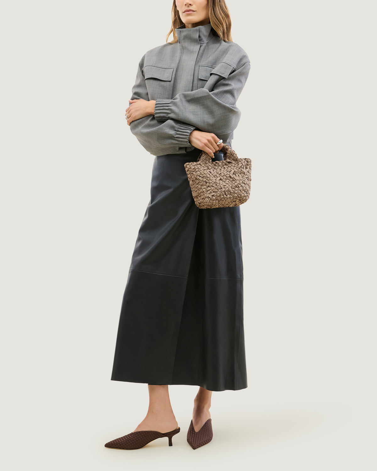 Model holding a cool taupe woven basket-style neoprene handbag with a top handle.