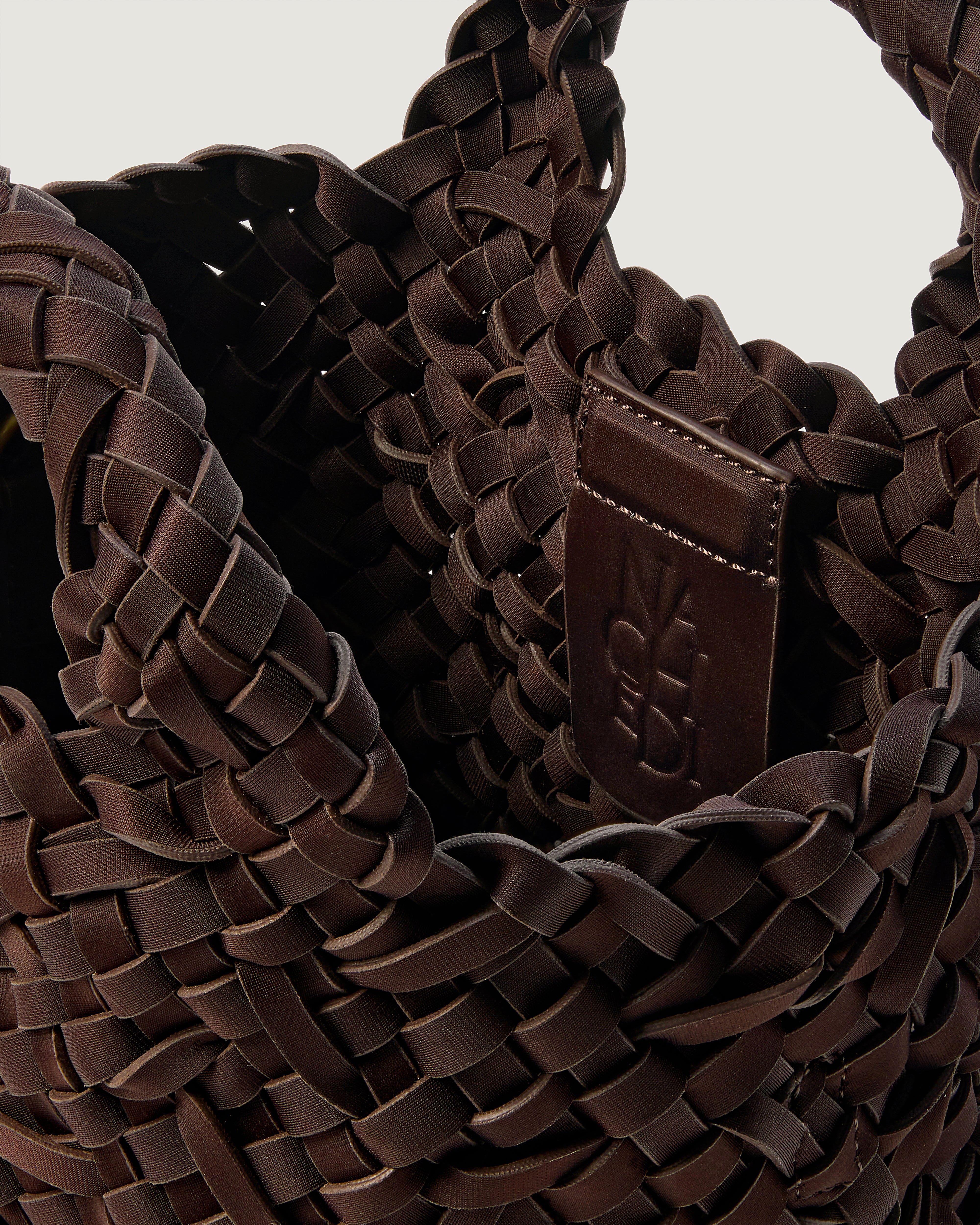 Close-up of a chocolate brown woven basket-style neoprene handbag with a top handle and a leather shoulder strap.