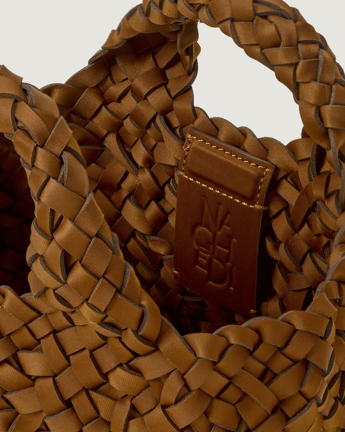 Close-up of a saddle brown woven basket-style neoprene handbag with a top handle and a leather shoulder strap.