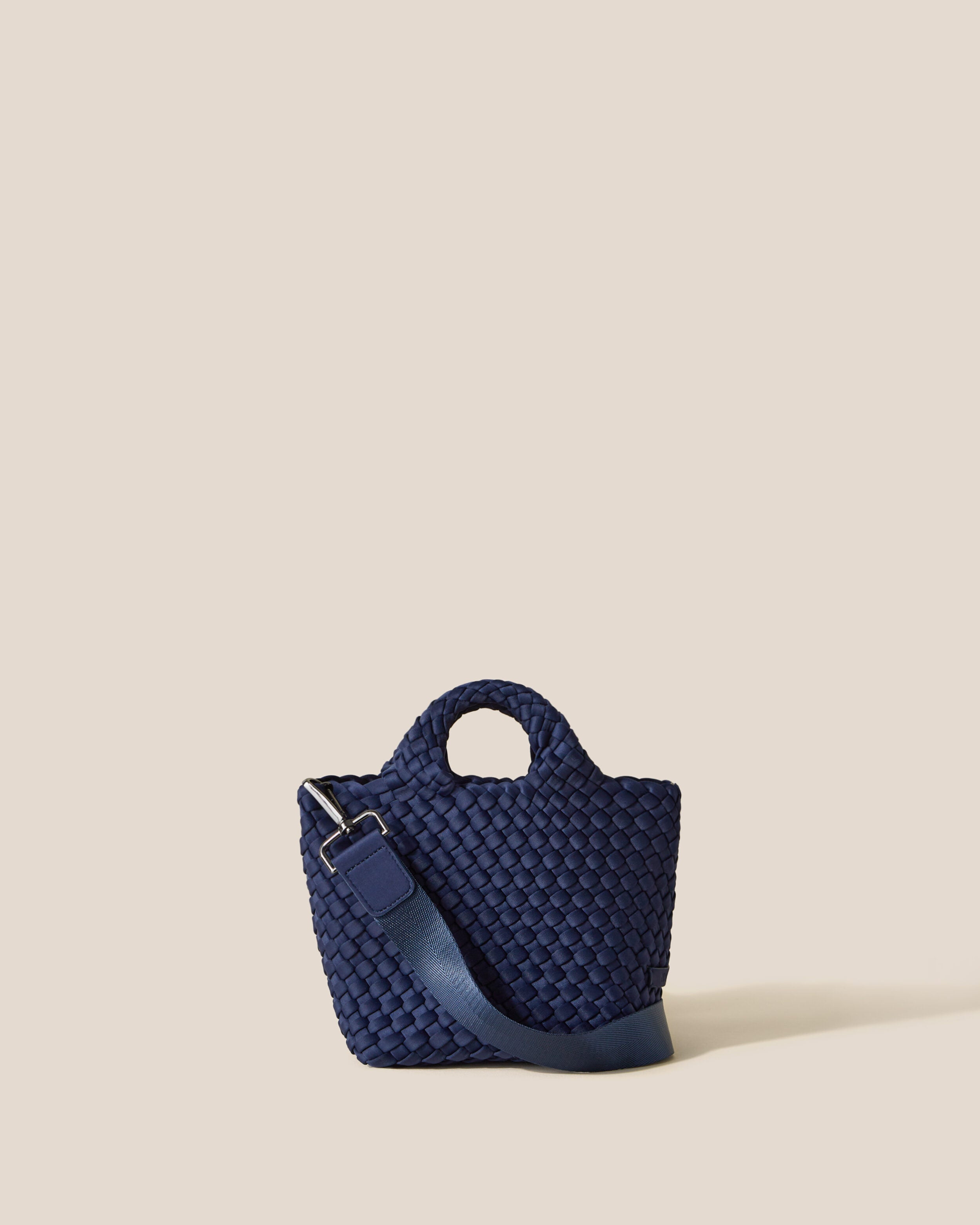 St. Barths Tote in Ink Blue, a navy blue tone, in handwoven neoprene, featuring an open top, woven top handles, and detachable, adjustable nylon crossbody strap.